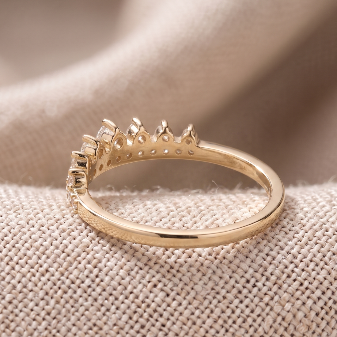 A gold ring with a crown-like top setting, photographed close-up on a textured beige fabric surface.