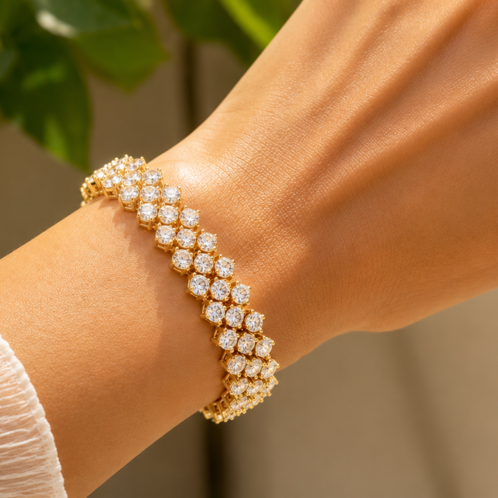 A close-up of a gold tennis bracelet with pavé-set clear stones worn on a person's wrist, with a softly blurred background.