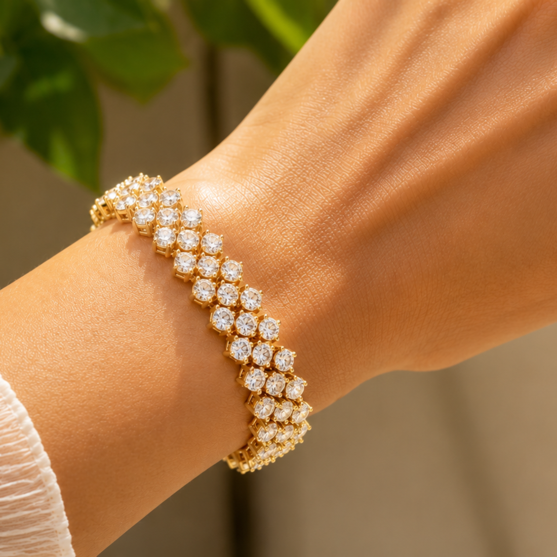 A close-up of a gold tennis bracelet with pavé-set clear stones worn on a person's wrist, with a softly blurred background.