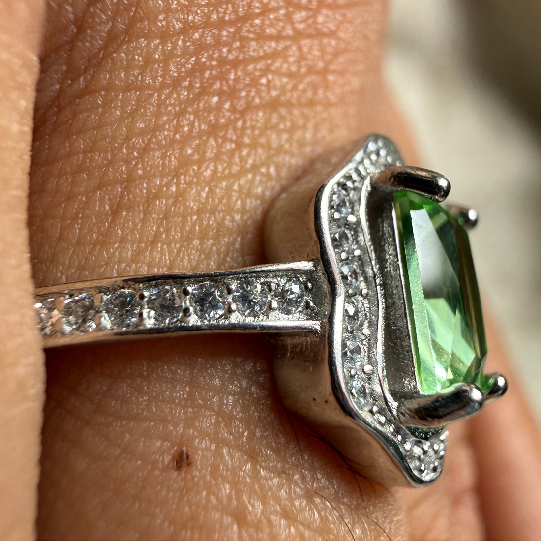 A sterling silver ring with a green emerald-cut gemstone and small clear accent stones, shown worn on a finger.