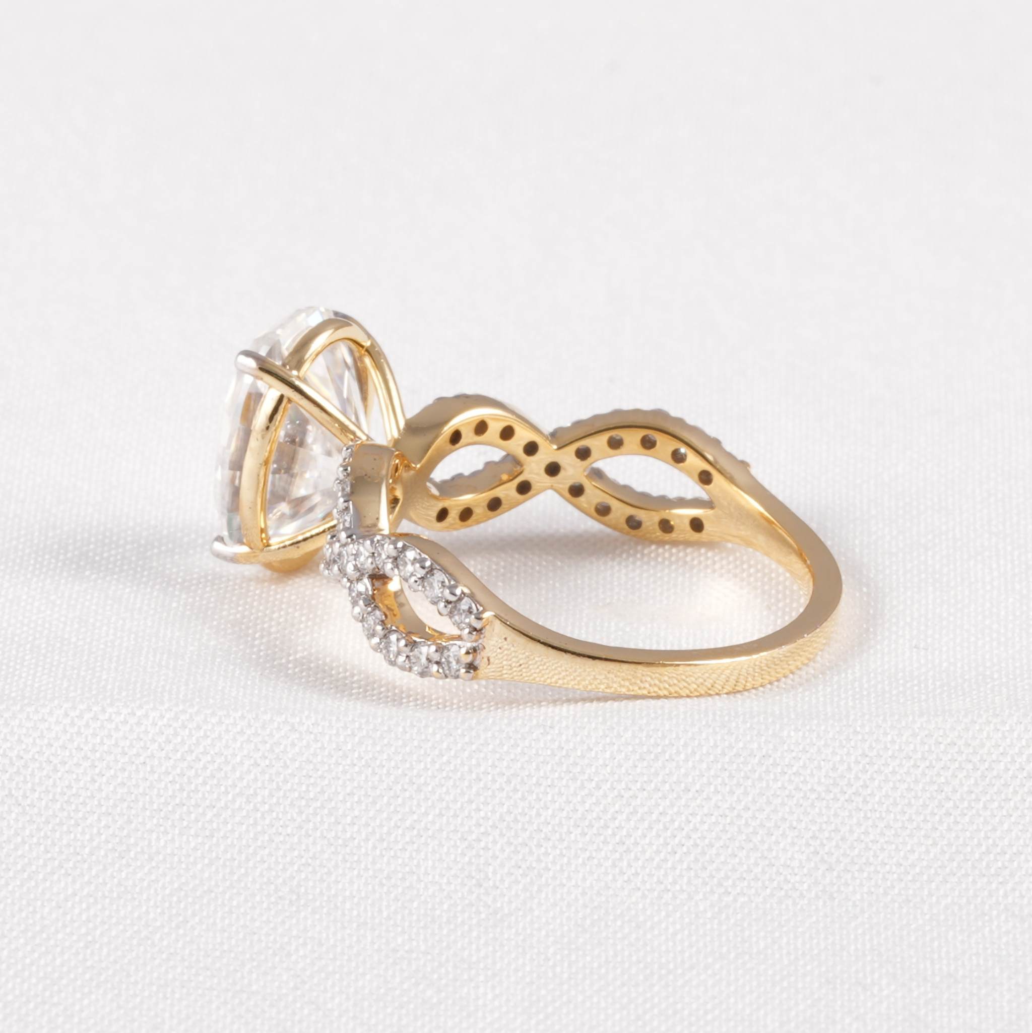 A gold ring with a large clear marquise-cut center stone and a curved band featuring small clear stones, photographed on a light textured white background.