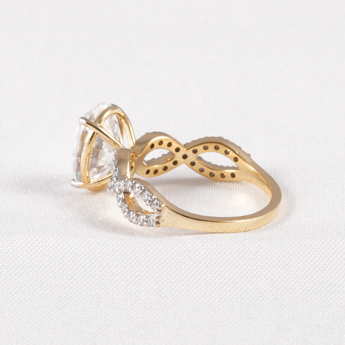 A gold ring with a large clear marquise-cut center stone and a curved band featuring small clear stones, photographed on a light textured white background.