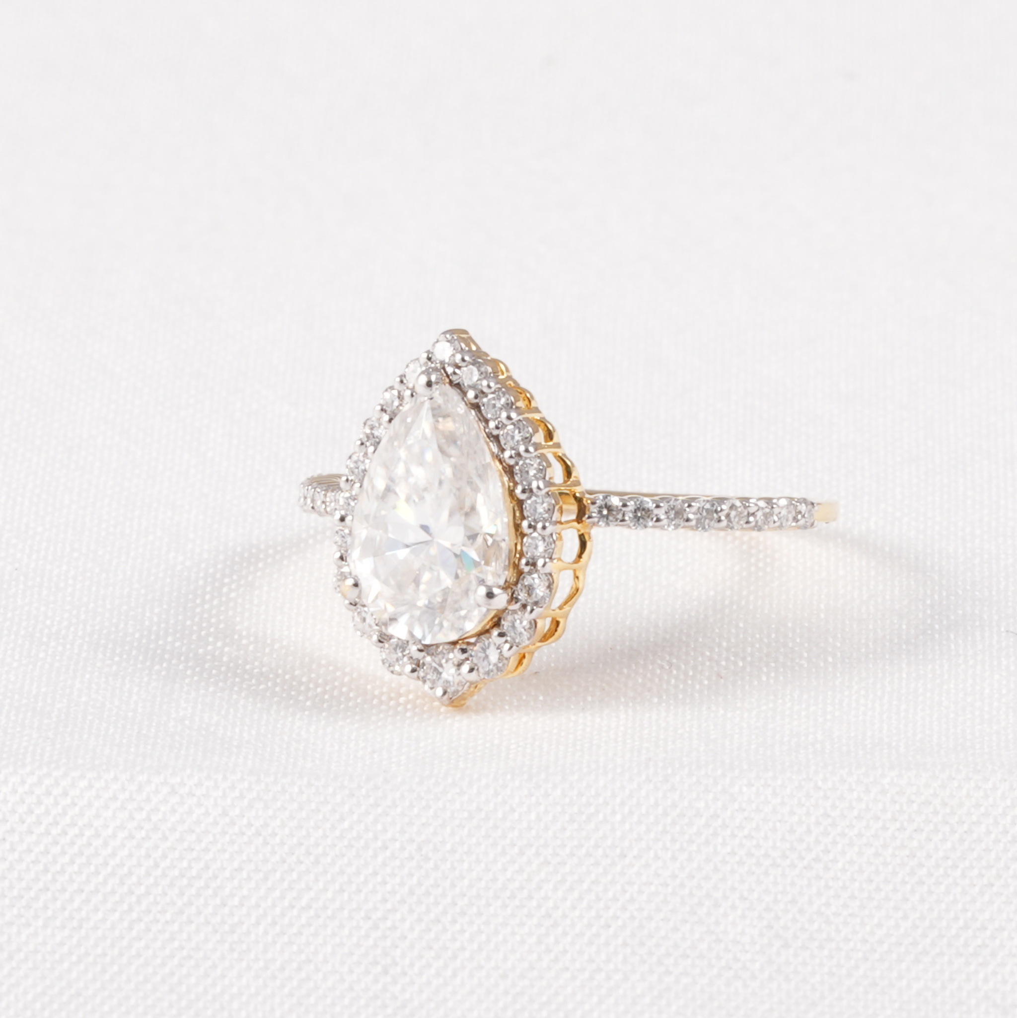A pear-cut diamond ring with a halo of small diamonds and a yellow gold band, set against a clean white textured background.