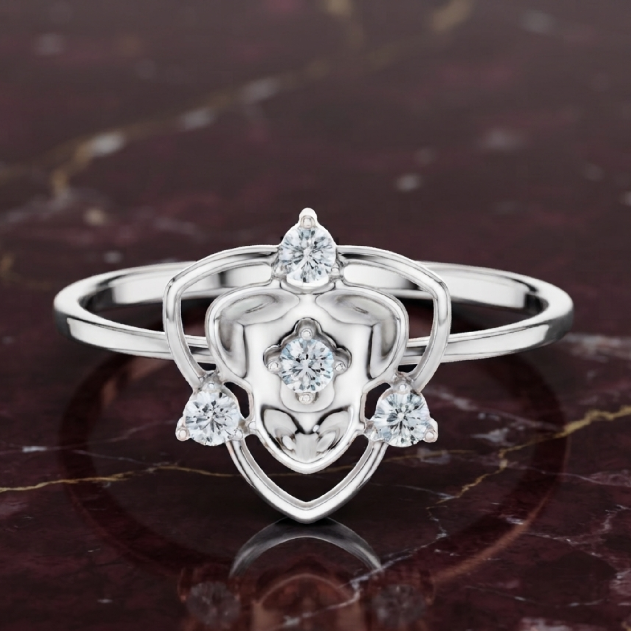 A silver ring with a heart-shaped openwork design and three clear gemstones, displayed on a dark marbled surface.