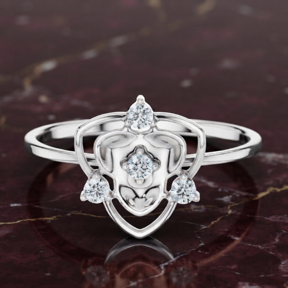 A silver ring with a heart-shaped openwork design and three clear gemstones, displayed on a dark marbled surface.