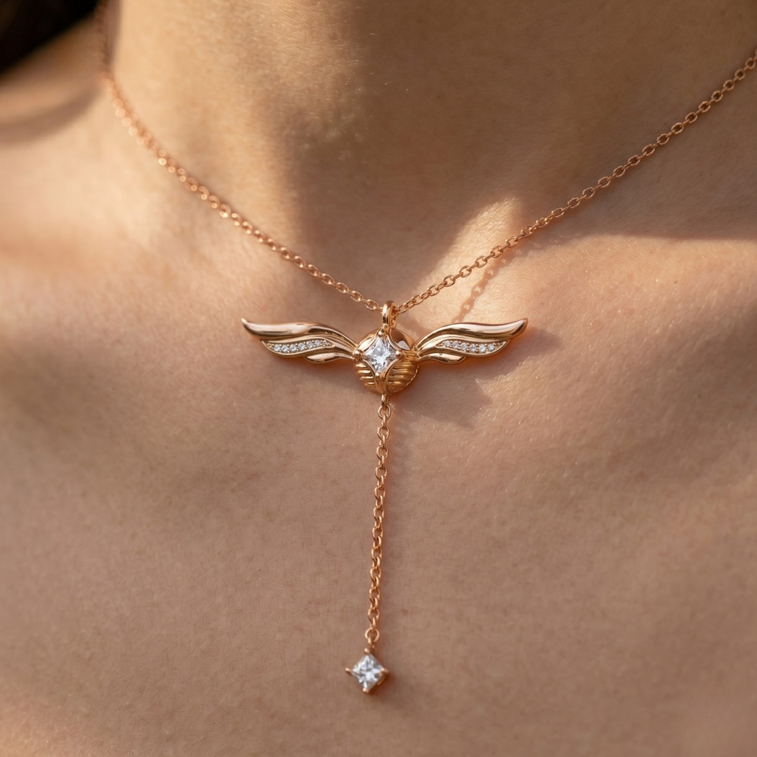 A close-up of a person's neck and upper chest wearing a delicate rose gold Y-necklace with wing-shaped pendants and clear gemstones.