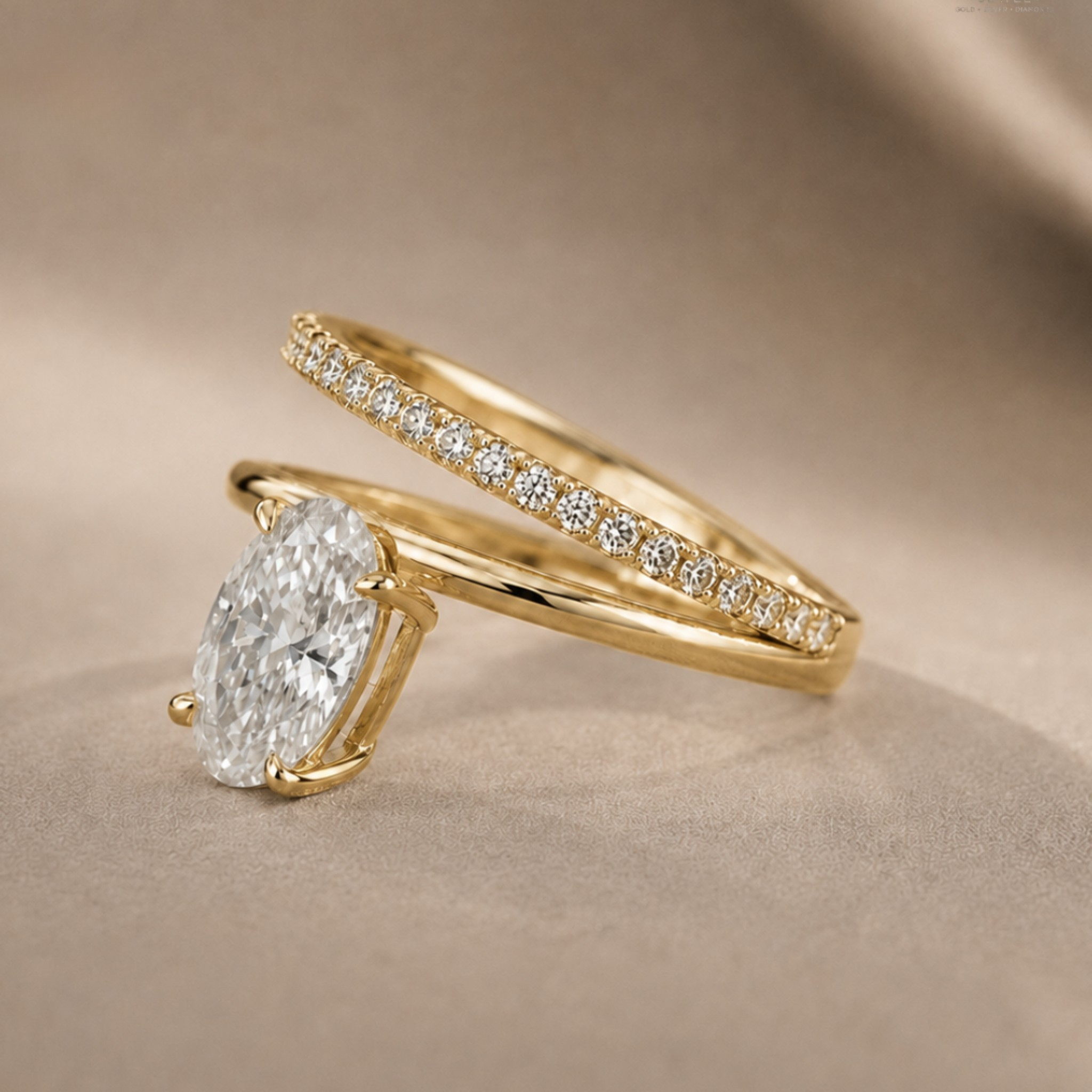 A gold engagement ring with a large oval-cut diamond and a matching pavé band ring, displayed on a soft beige fabric background.