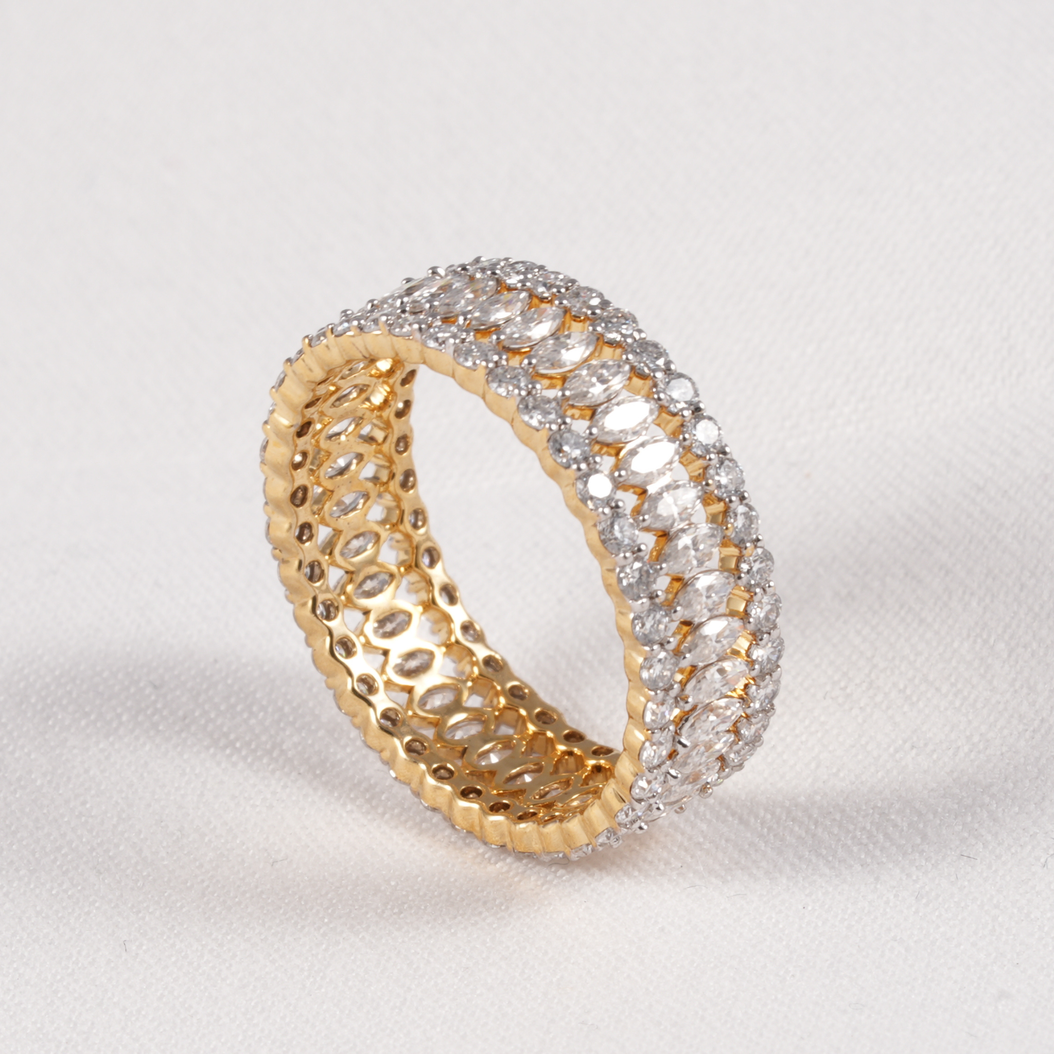A yellow gold eternity ring set with clear cubic zirconia stones, photographed on a textured off-white background.