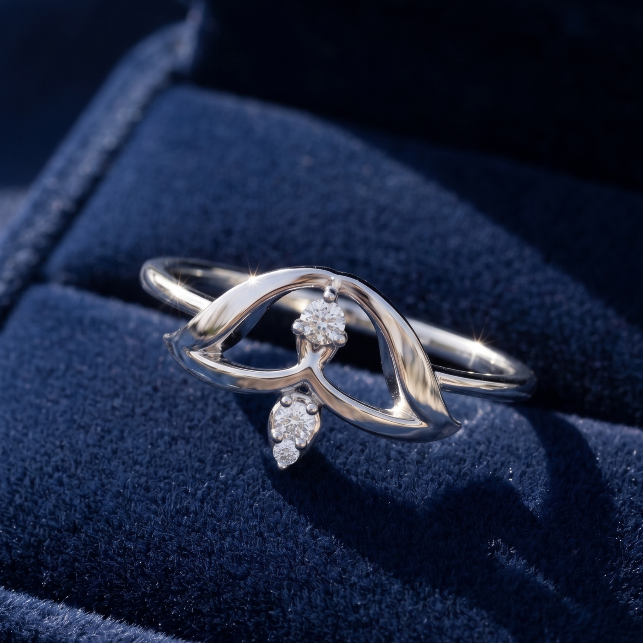 A silver ring with a sculptural, flowing openwork design and small clear gemstones, displayed on a dark blue velvet jewelry box.