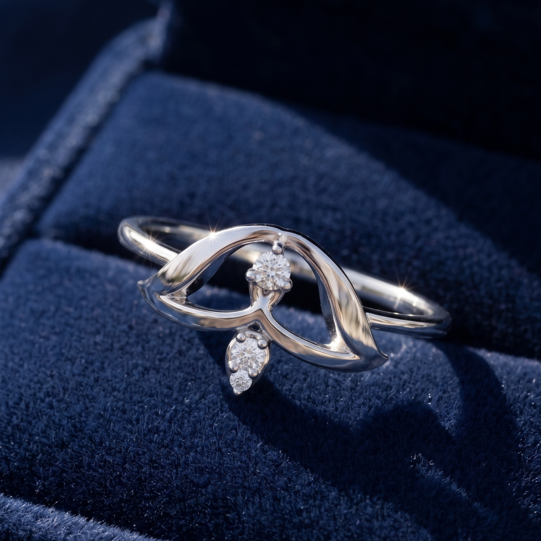 A silver ring with a sculptural, flowing openwork design and small clear gemstones, displayed on a dark blue velvet jewelry box.