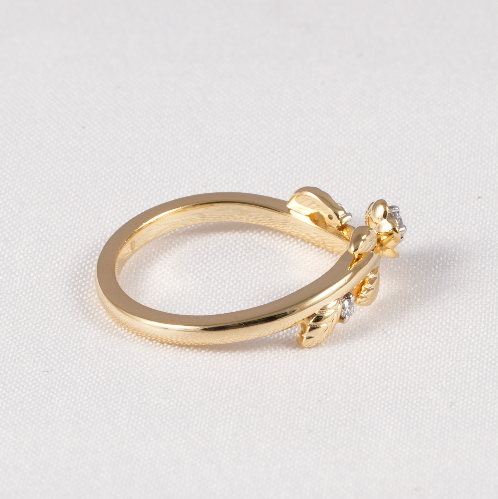 A yellow gold ring featuring a small floral cluster with clear gemstones on the band, photographed on a textured white background.