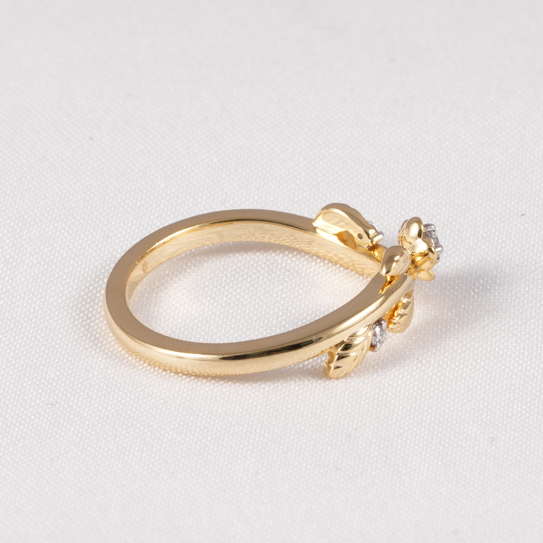 A yellow gold ring featuring a small floral cluster with clear gemstones on the band, photographed on a textured white background.