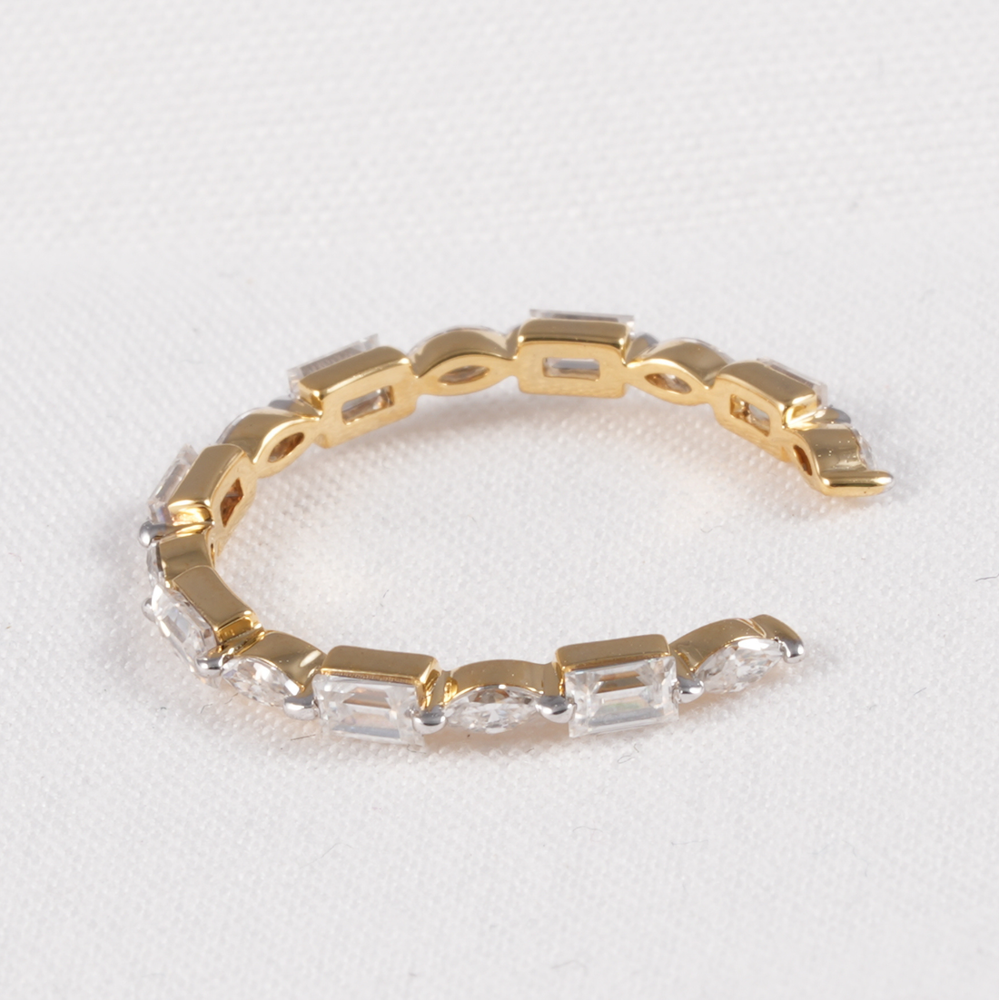A gold-plated open cuff bracelet featuring a row of clear rectangular baguette-cut crystals, displayed on a textured white background.