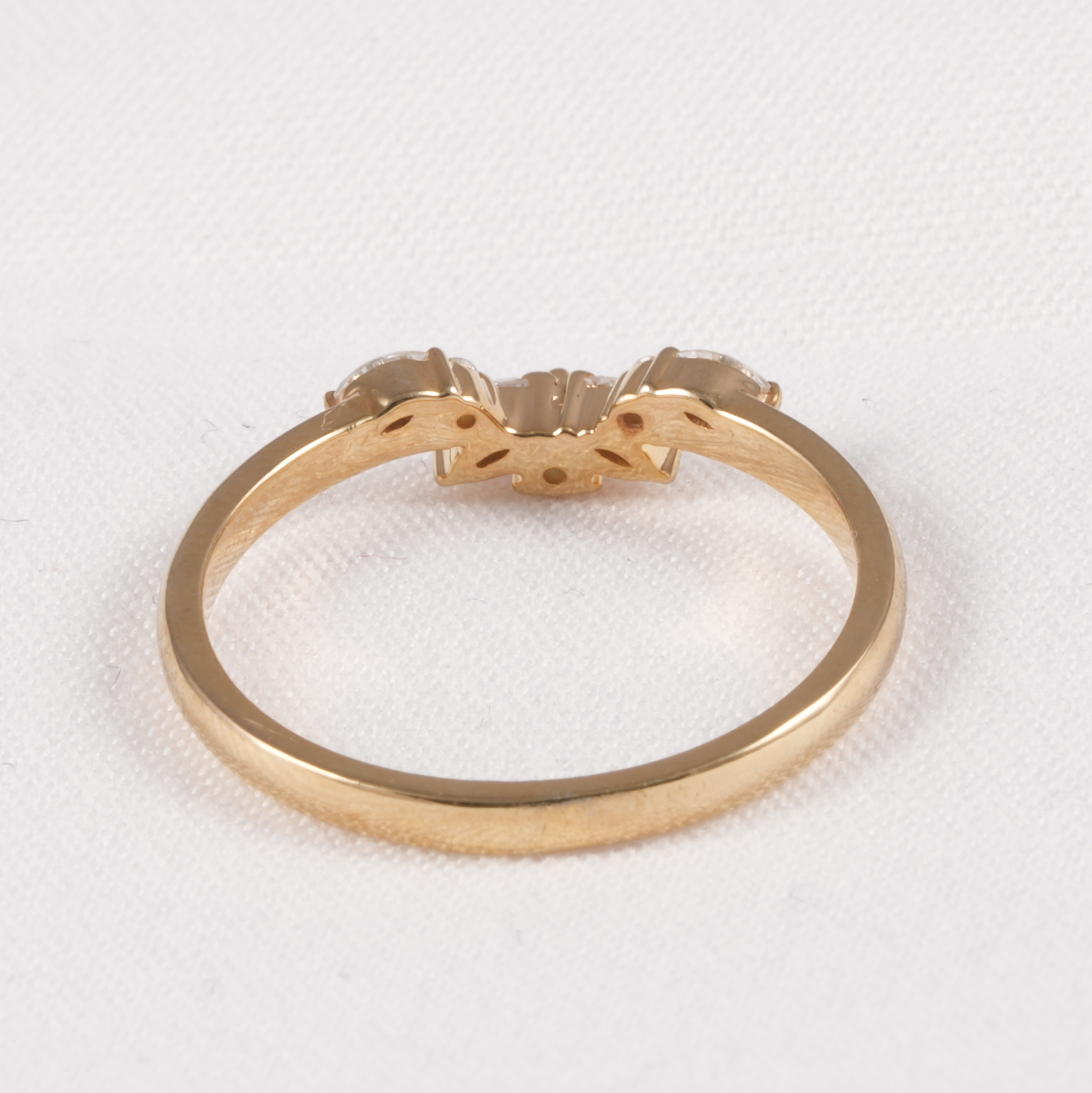 A yellow gold ring with a decorative three-stone cluster setting, photographed on a textured white background.