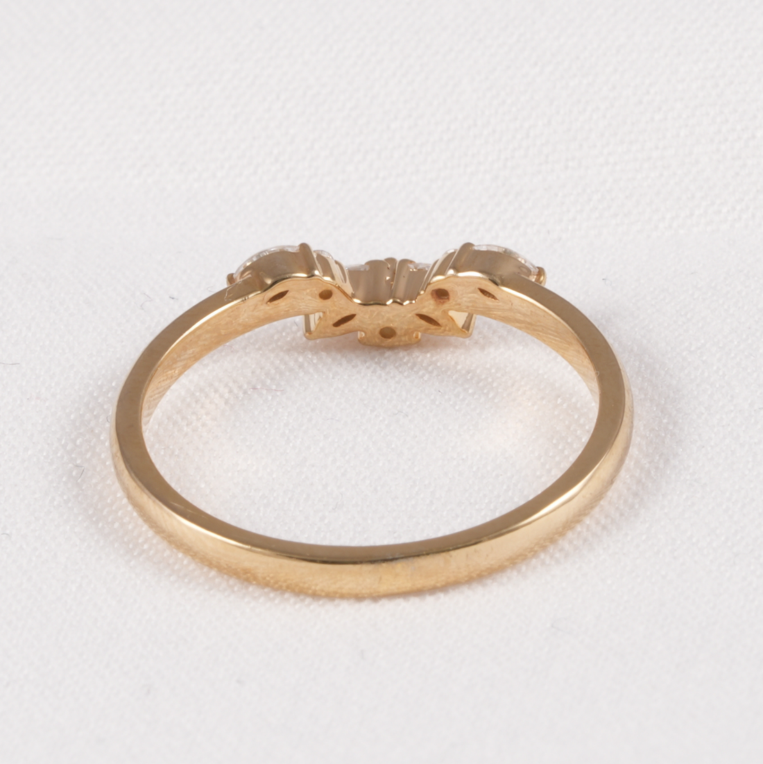 A yellow gold ring with a decorative three-stone cluster setting, photographed on a textured white background.