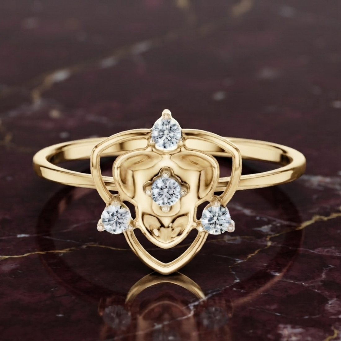 A yellow gold ring with an intricate shield-like openwork design and three clear gemstones, displayed on a dark marbled surface.