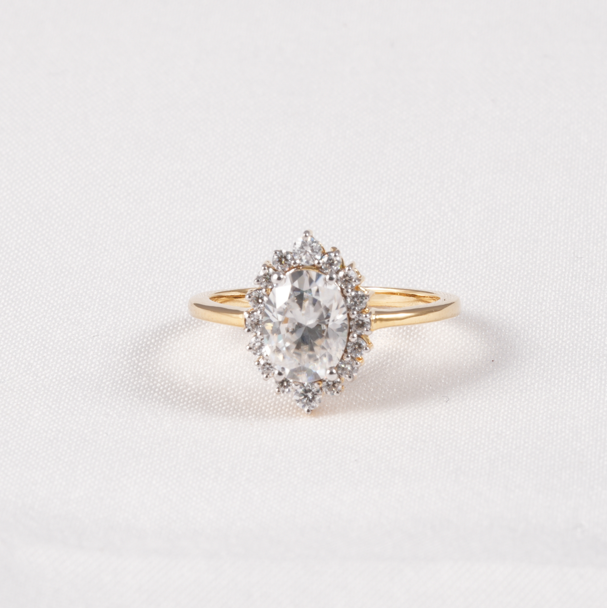 A yellow gold ring featuring a pear-cut clear gemstone in a halo setting with smaller round stones, photographed on a textured white background.