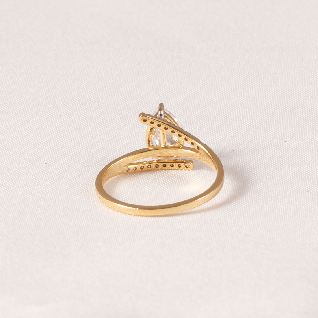 A gold ring with a triangular cluster setting and a clear central gemstone, photographed on a light beige textured fabric background.
