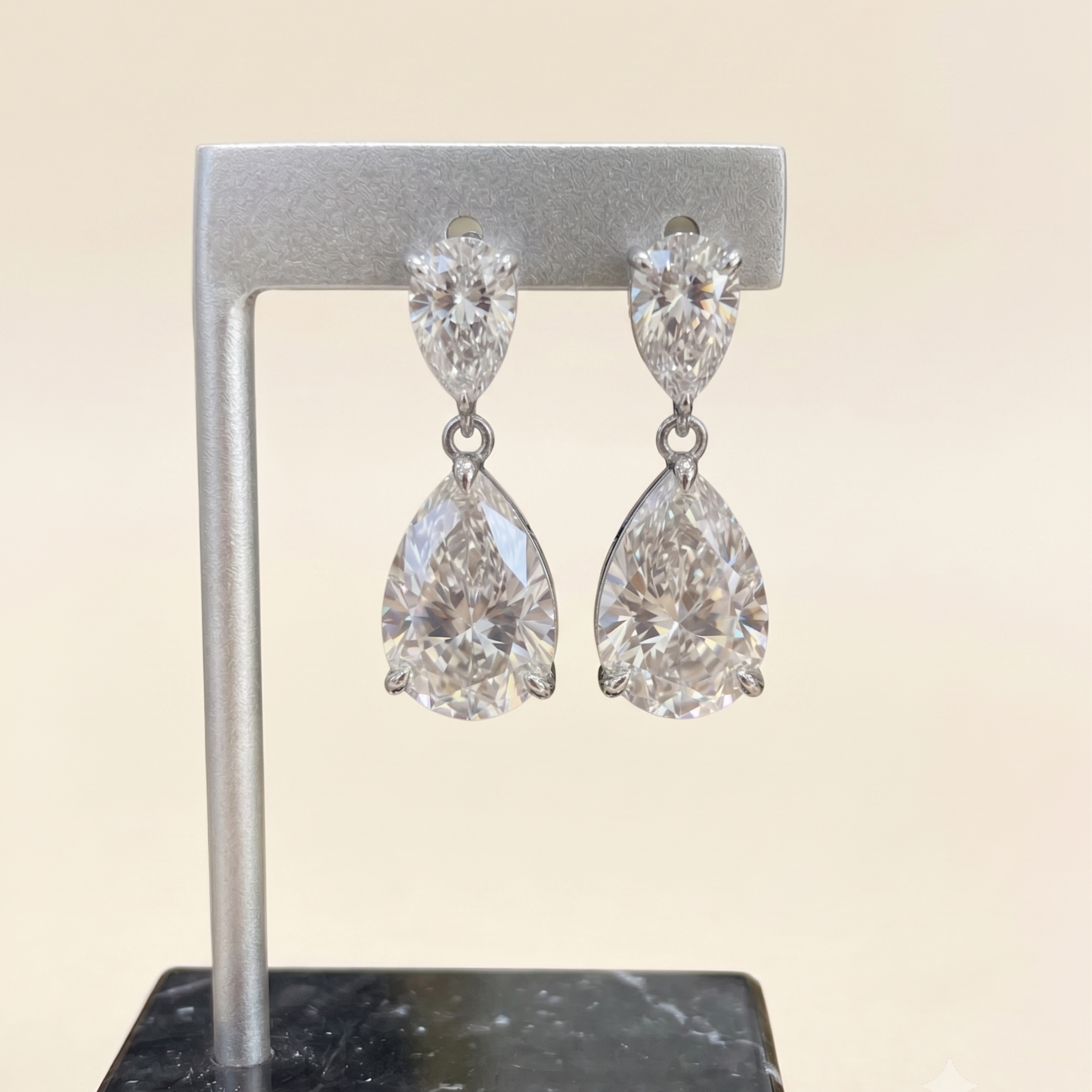 A pair of silver-tone drop earrings with marquise-cut and pear-cut clear gemstones, displayed on a silver stand against a light beige background.