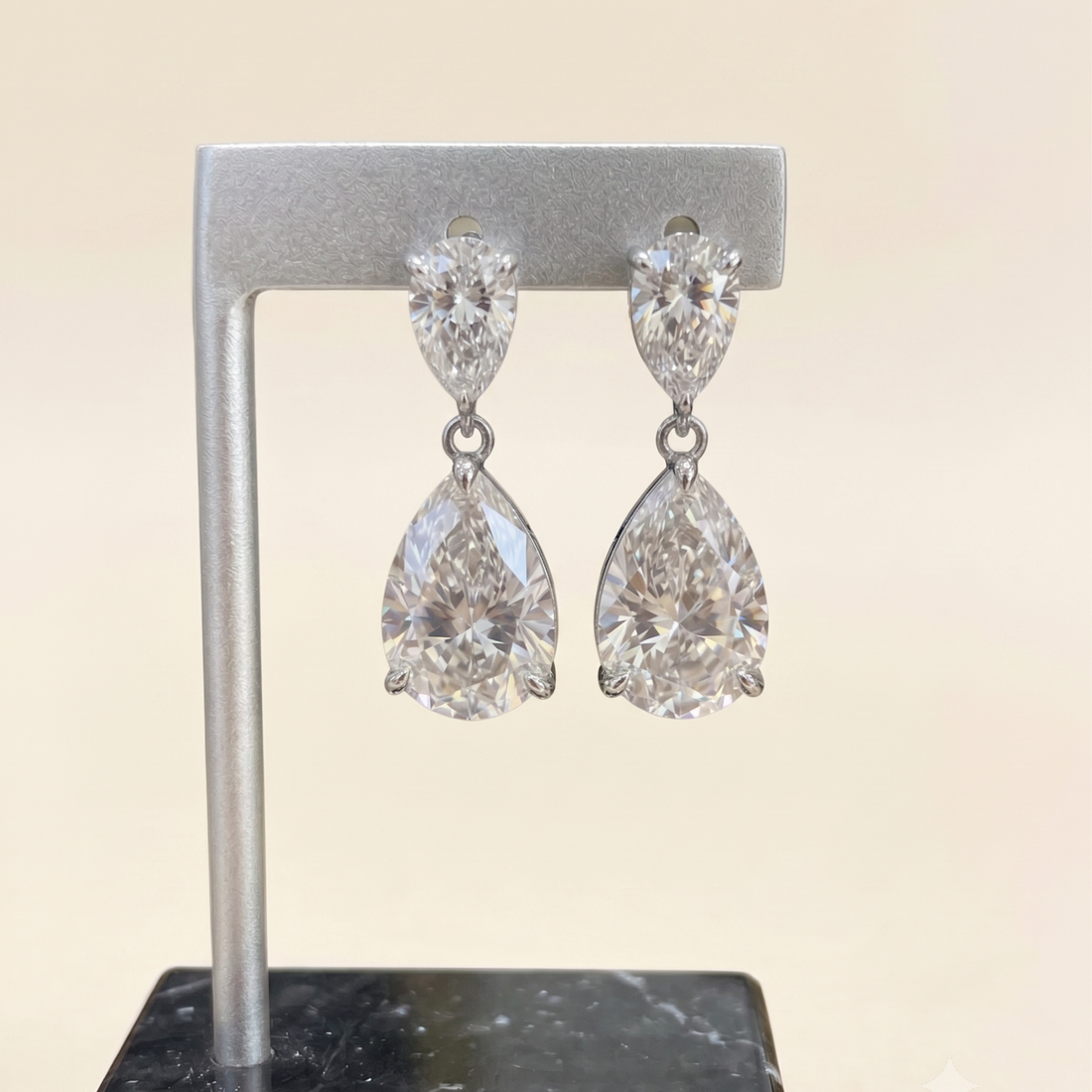 A pair of silver-tone drop earrings with marquise-cut and pear-cut clear gemstones, displayed on a silver stand against a light beige background.