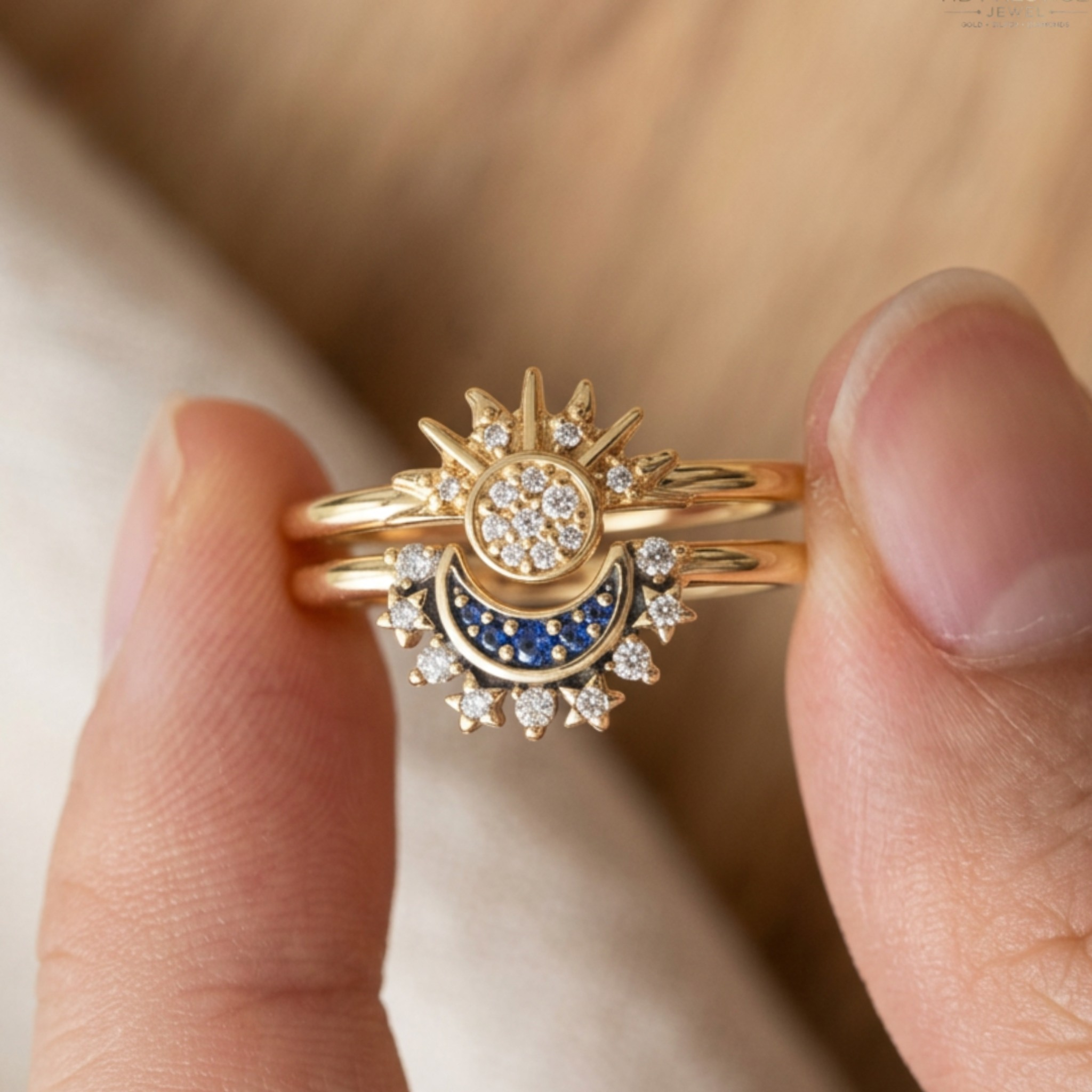 A close-up of a gold ring with a sun and crescent moon design, featuring blue and clear stones, held between two fingers.