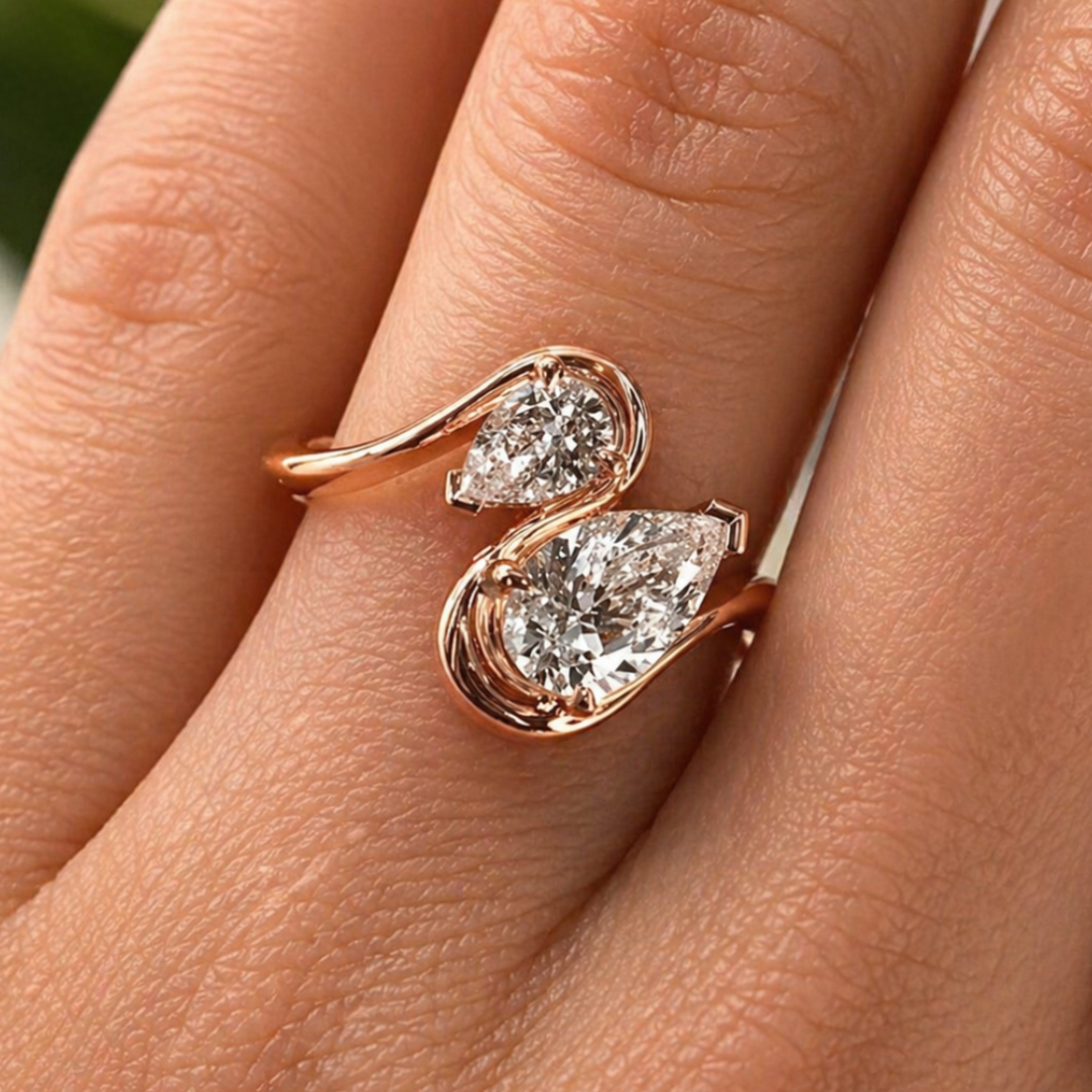 A close-up of a rose gold ring with two pear-cut clear gemstones on a person's finger.