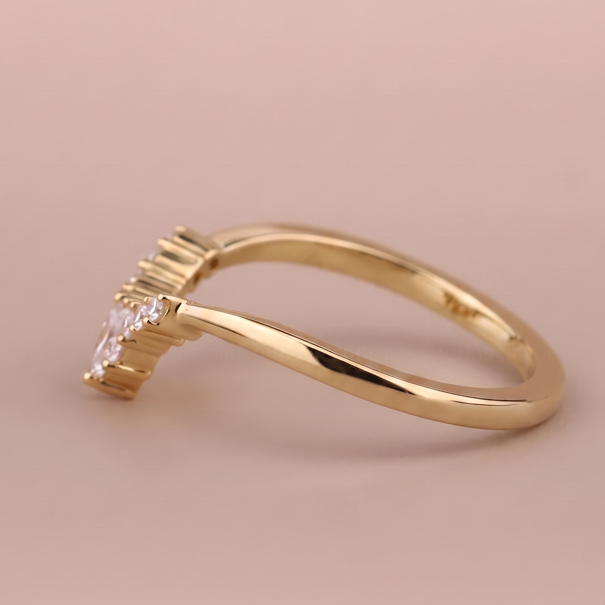 A gold ring with a curved band and a small clear gemstone in a prong setting, photographed on a soft beige background.