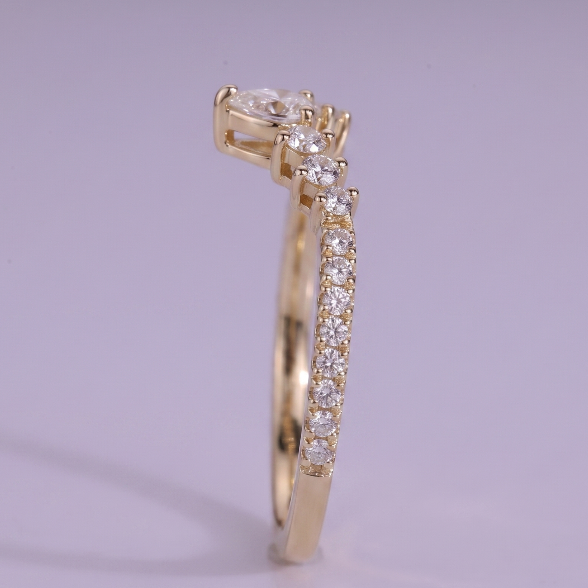 A yellow gold ring featuring a round-cut center stone and a pavé band set with small clear stones, shown against a soft lavender background.