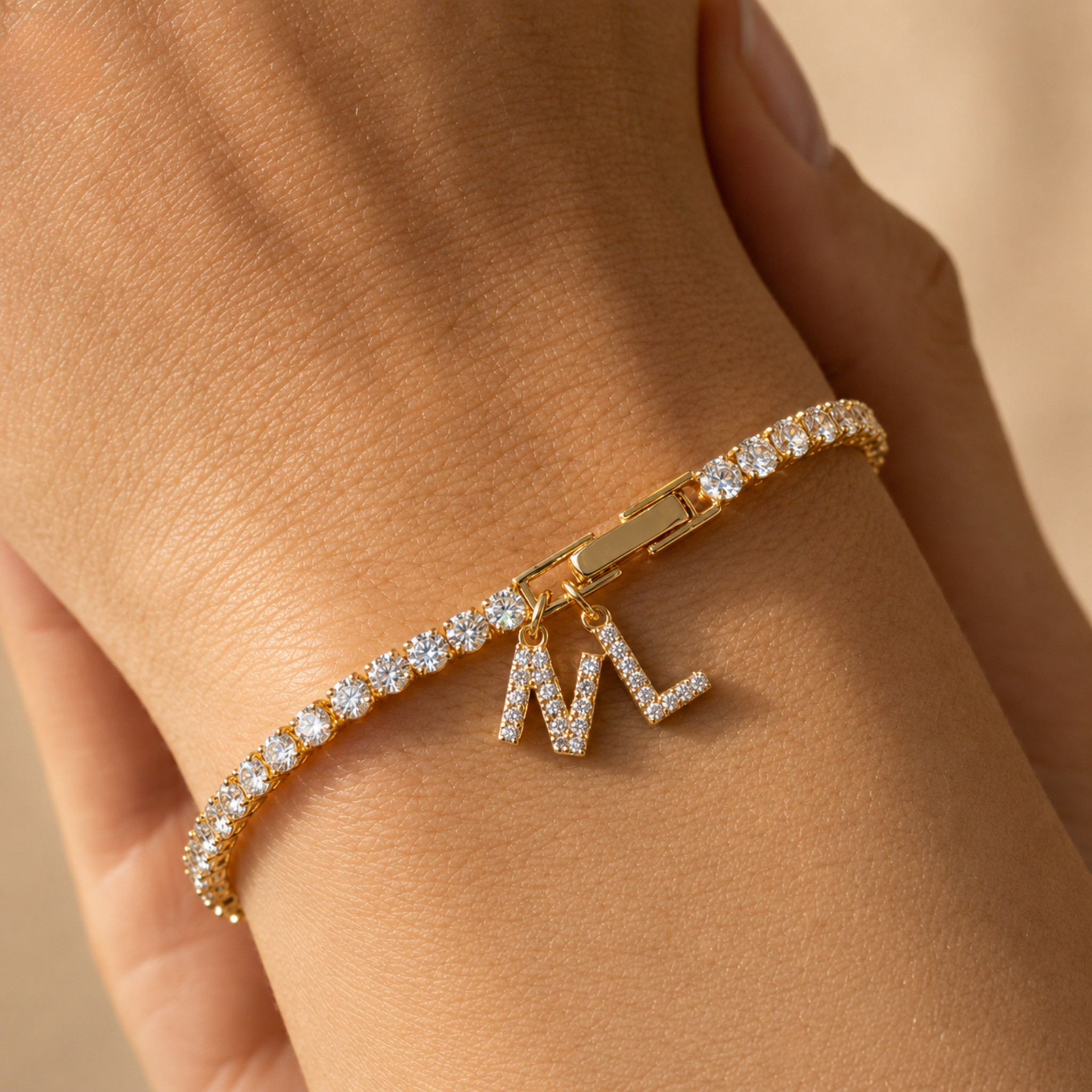 A gold bracelet with a row of clear pavé stones and a dangling initial charm reading 'ML', shown worn on a person's wrist.