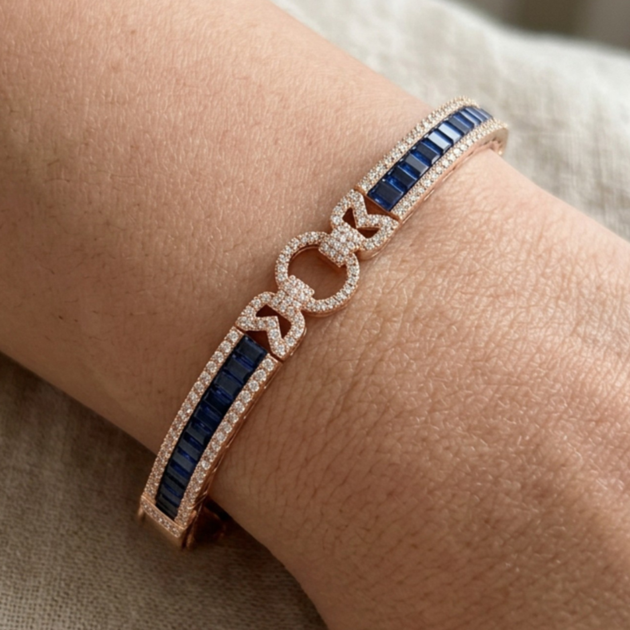 A close-up of a rose gold bracelet with deep blue baguette gemstones and pavé-set clear stones, shown worn on a wrist.