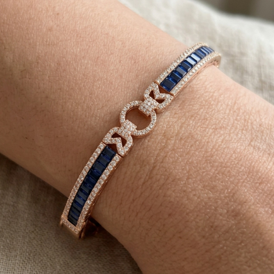 A close-up of a rose gold bracelet with deep blue baguette gemstones and pavé-set clear stones, shown worn on a wrist.