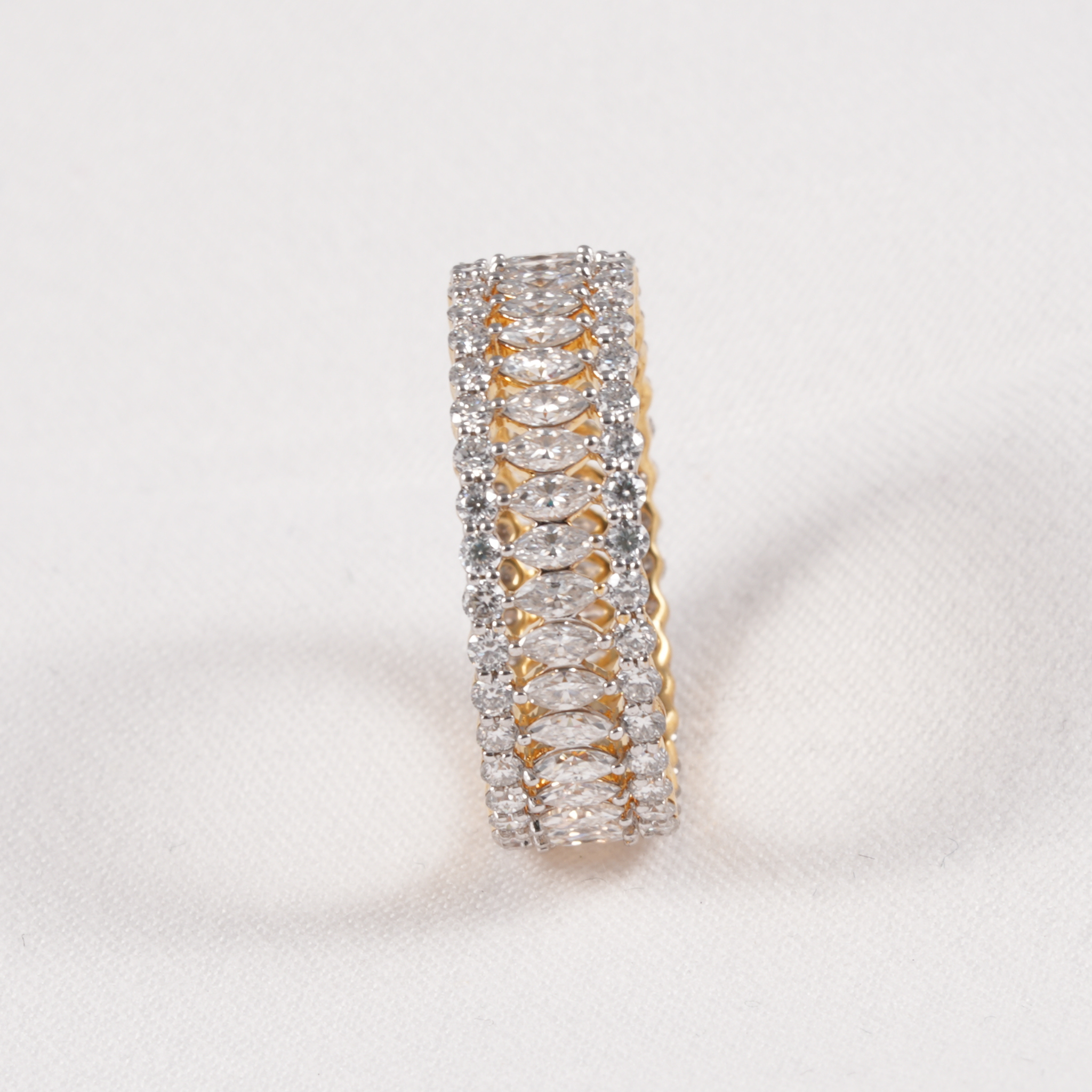 A gold eternity ring paved with clear marquise-cut gemstones, photographed on a clean white textured background.