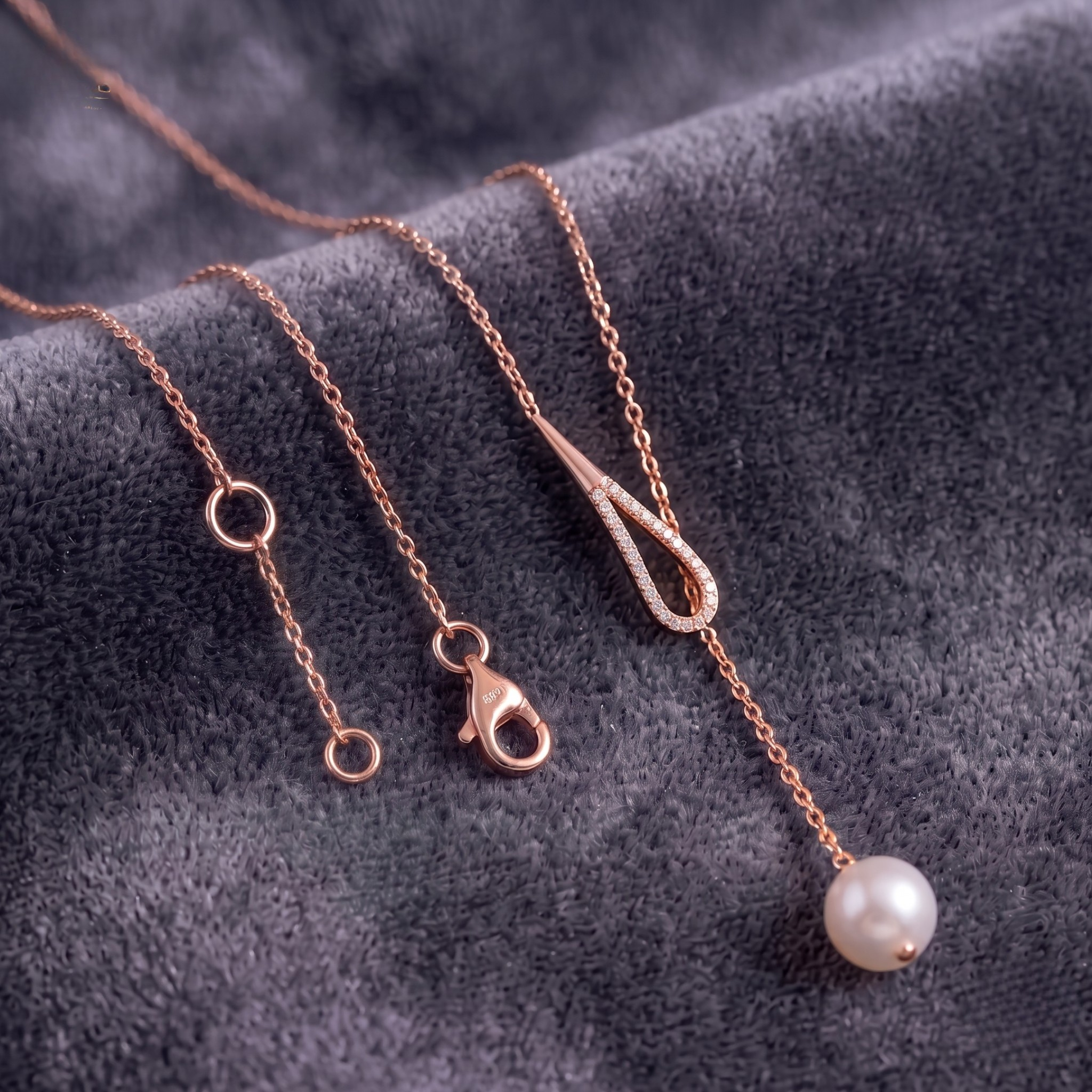 Rose gold chain necklace with a single white pearl drop pendant, displayed on a textured dark gray velvet background.