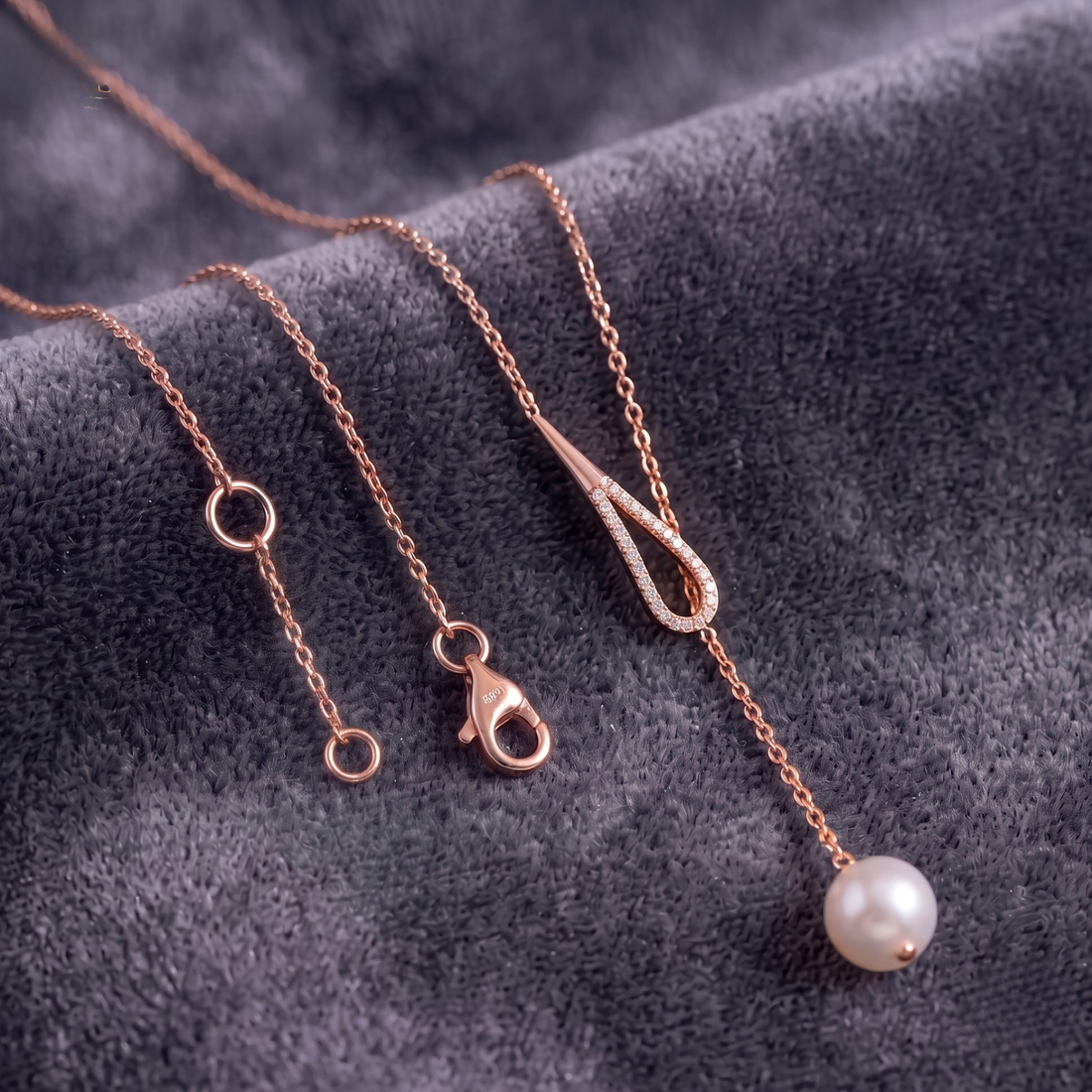 Rose gold chain necklace with a single white pearl drop pendant, displayed on a textured dark gray velvet background.
