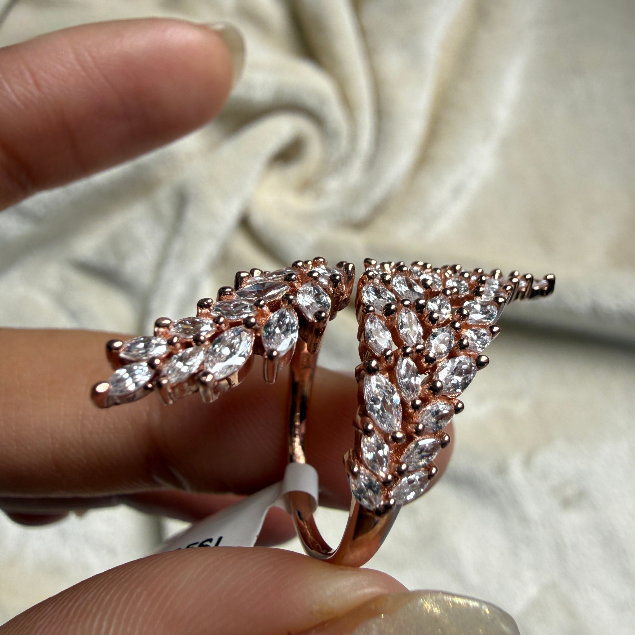 A rose gold ring with marquise-cut clear gemstones, held between fingers against a soft beige fabric background.