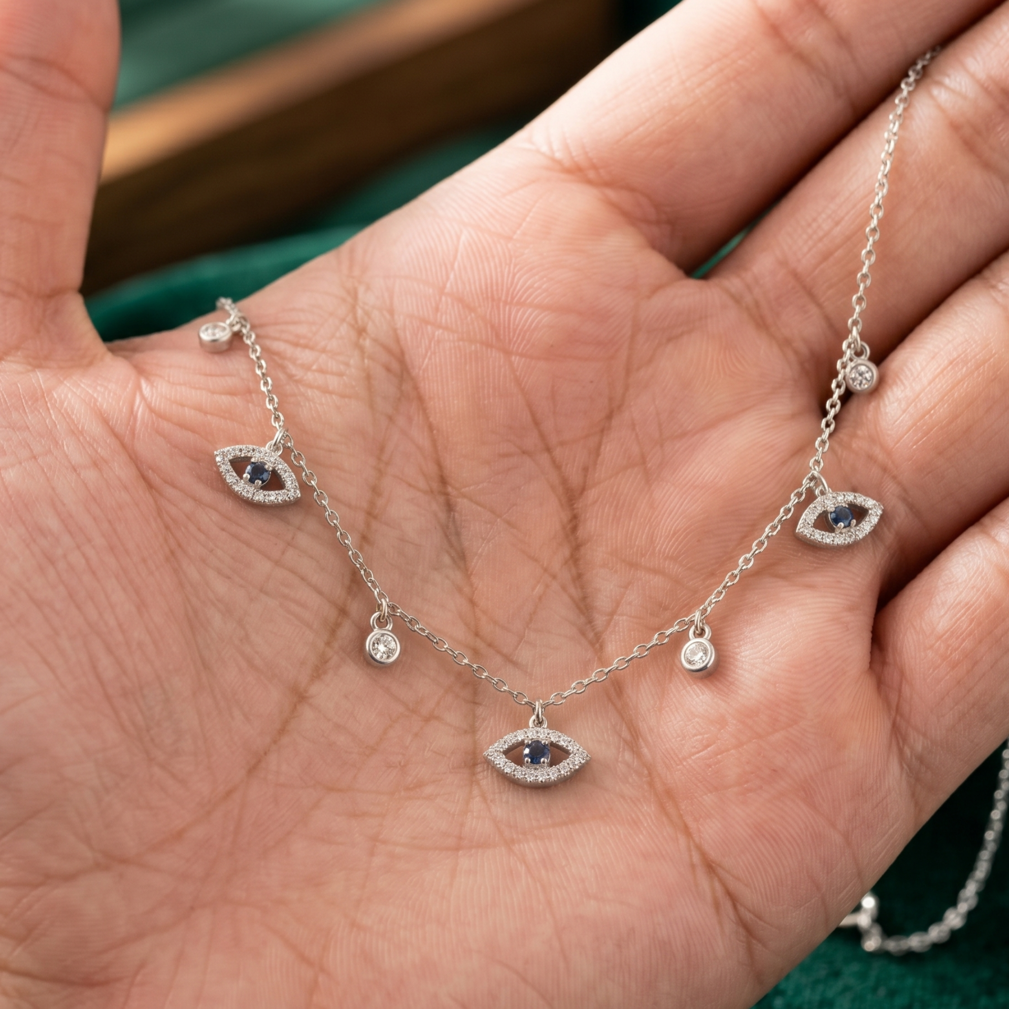 A silver-toned evil eye necklace with small clear stones and dark blue center gems, draped across an open hand.