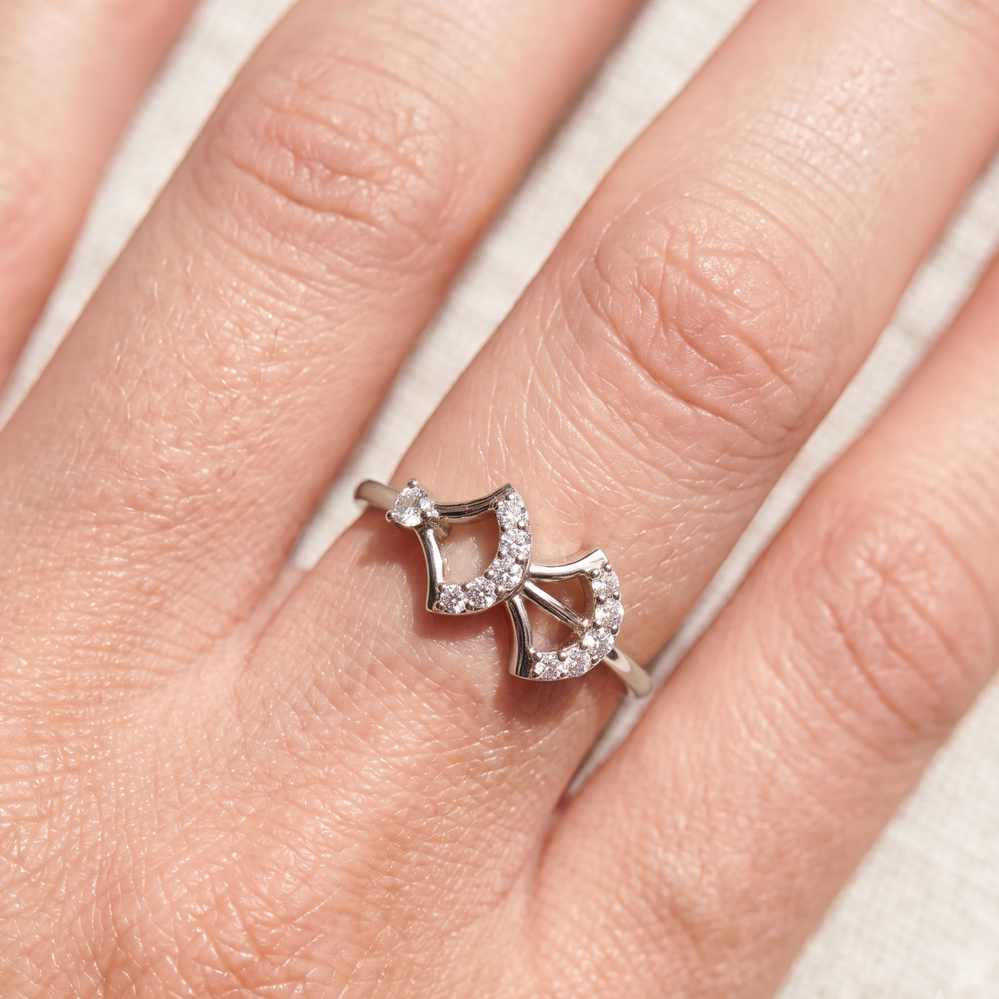 A silver ring with a double bow design set with small clear stones, shown worn on a finger.