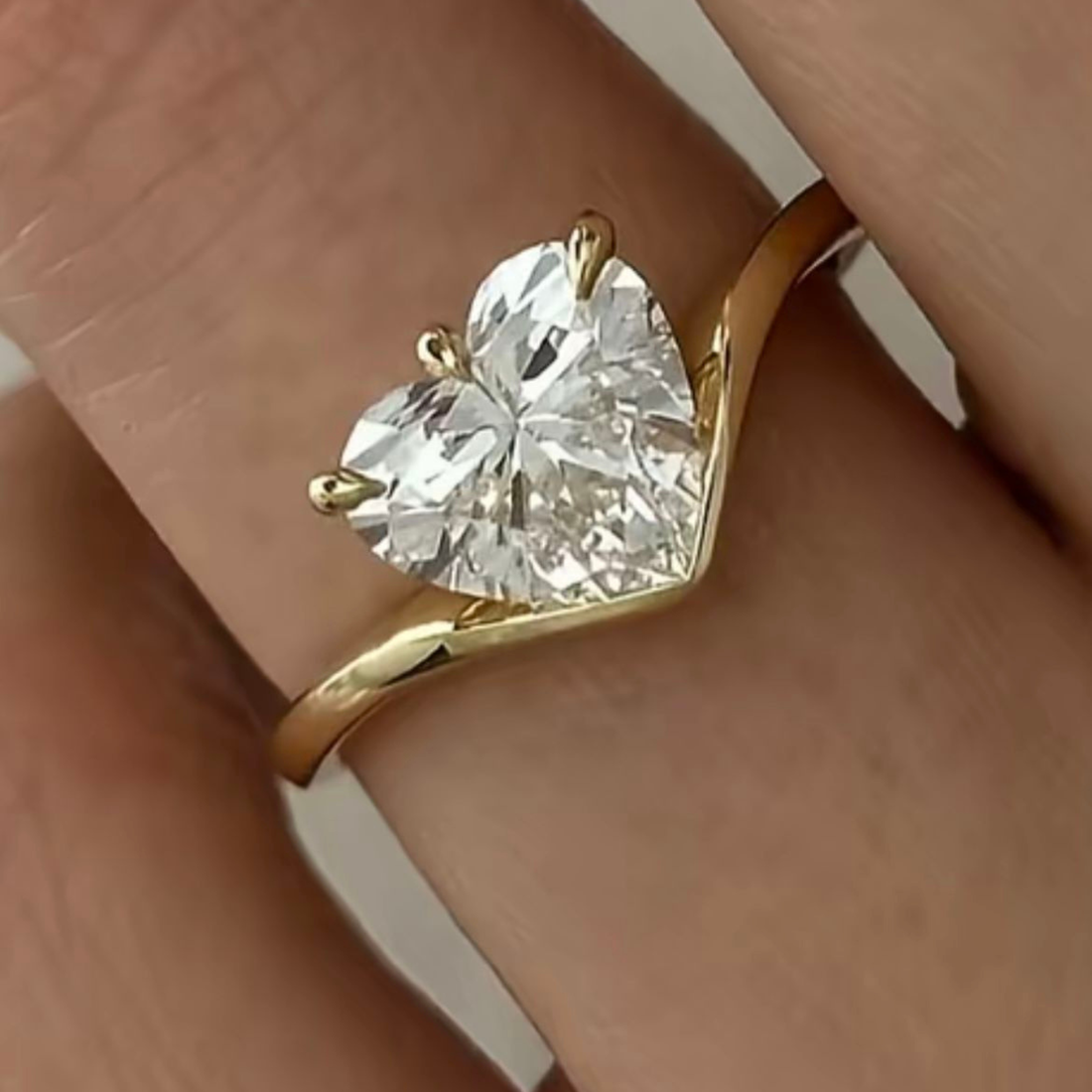 A heart-shaped diamond ring set in a yellow gold band, shown worn on a person's finger.