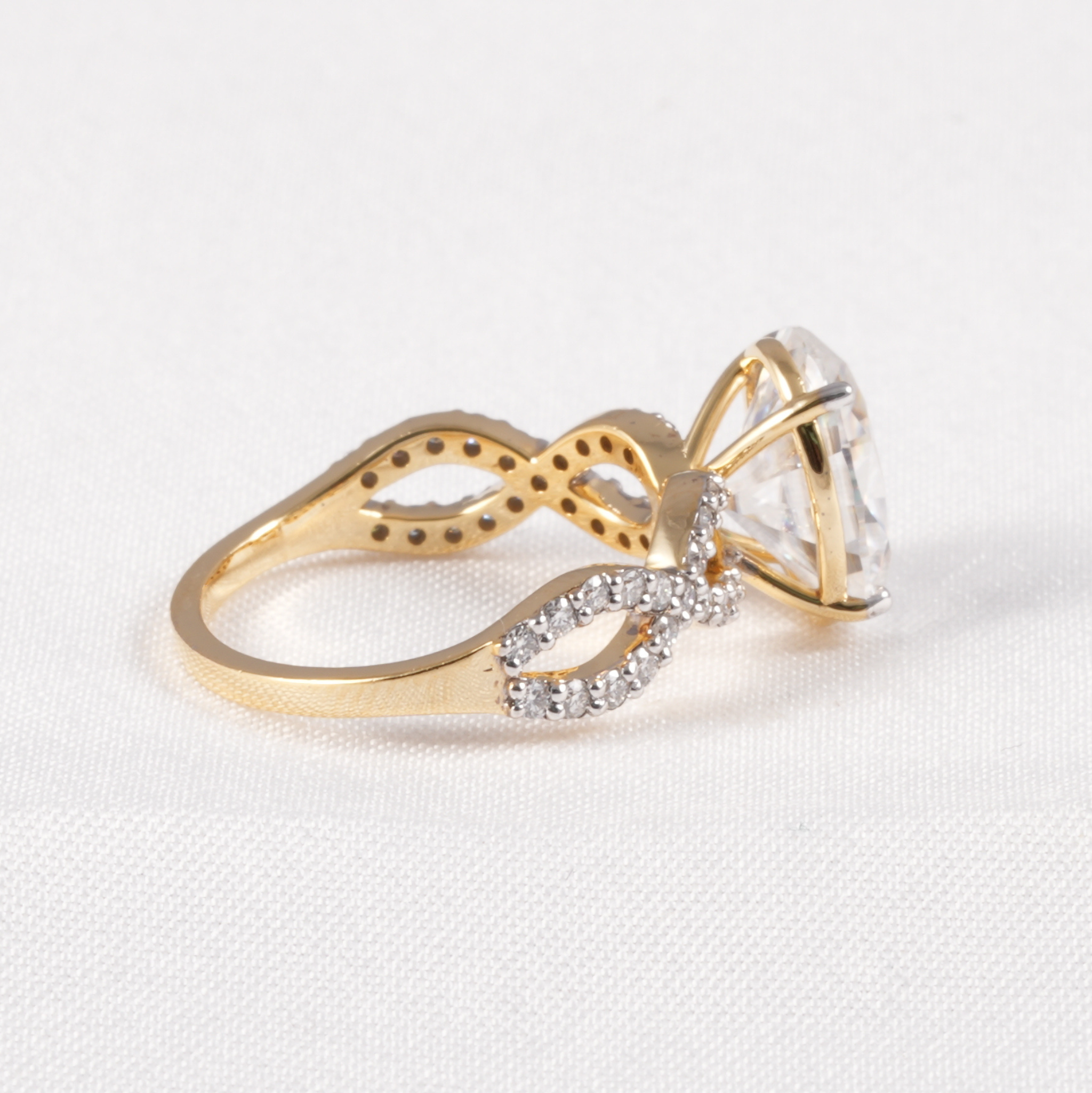 A gold ring with a large clear gemstone and pavé-set clear accent stones on a textured white background.