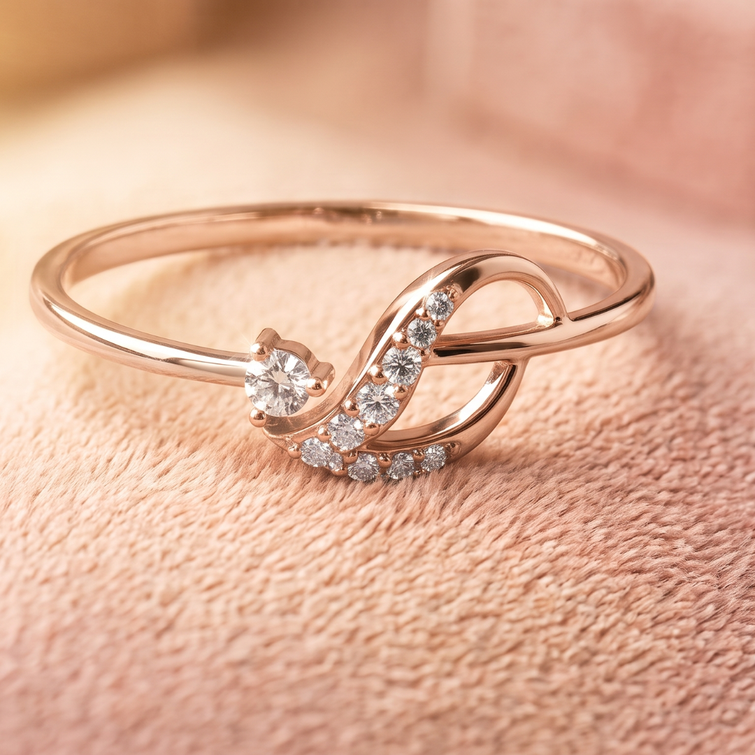 A rose gold ring with a twisted infinity symbol design, accented with small clear pavé stones and a single round center stone, resting on a textured pink fabric background.
