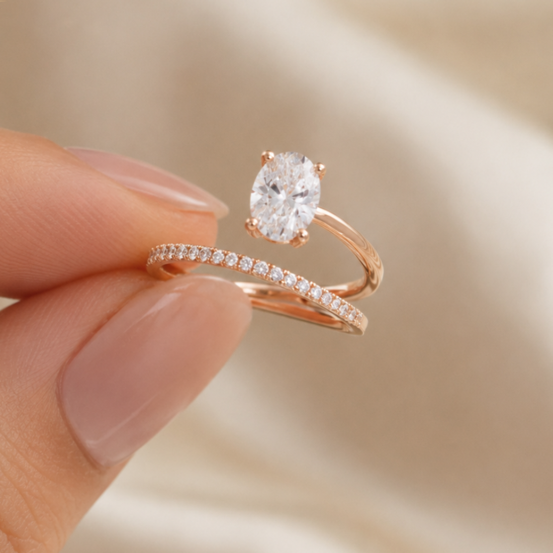 A rose gold engagement ring with a pear-cut clear center stone and a matching rose gold pavé band, held between fingers against a soft beige satin background.