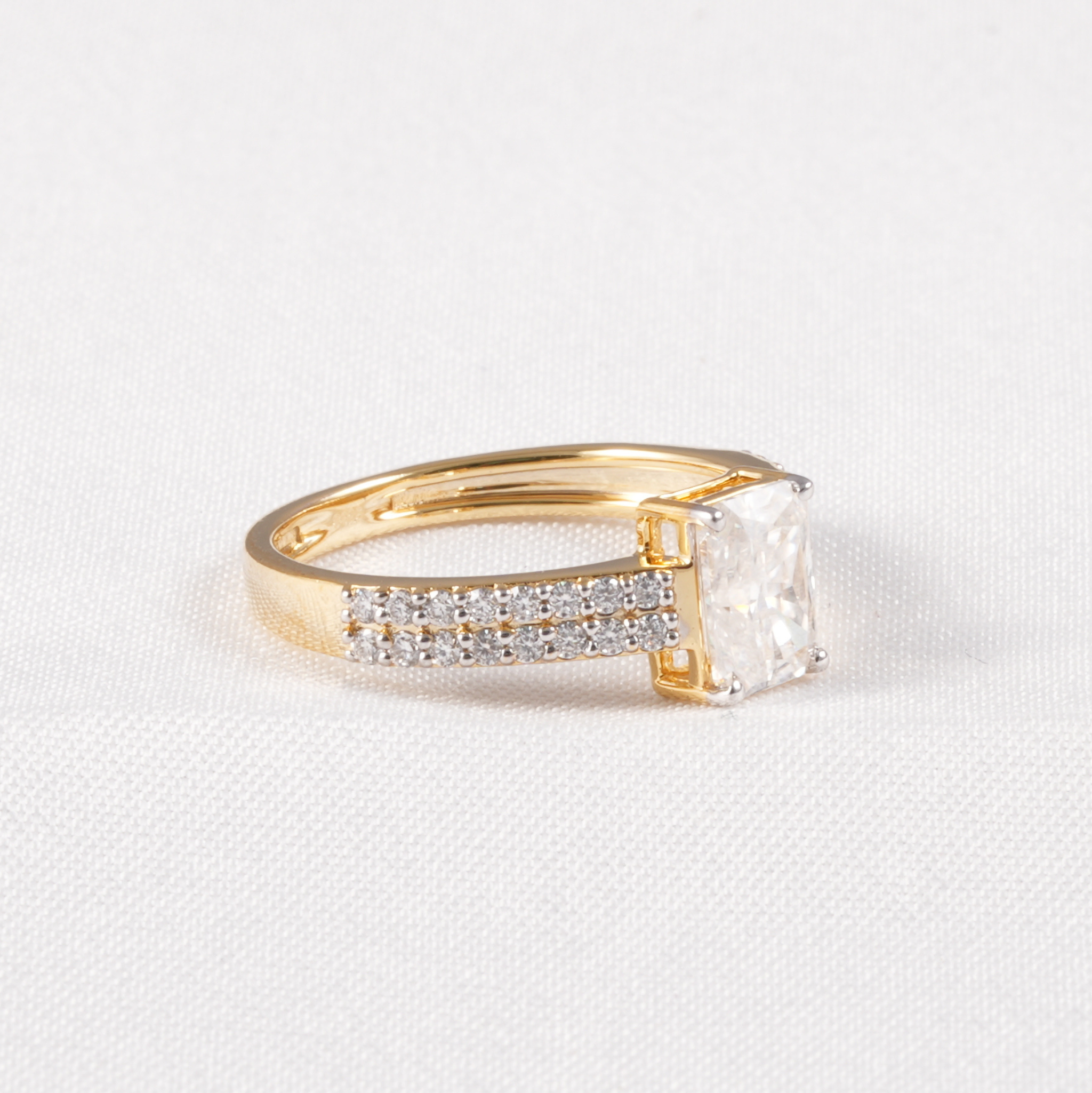 A yellow gold ring featuring a large rectangular clear gemstone and a row of small pavé-set clear stones on the band, photographed on a textured white background.