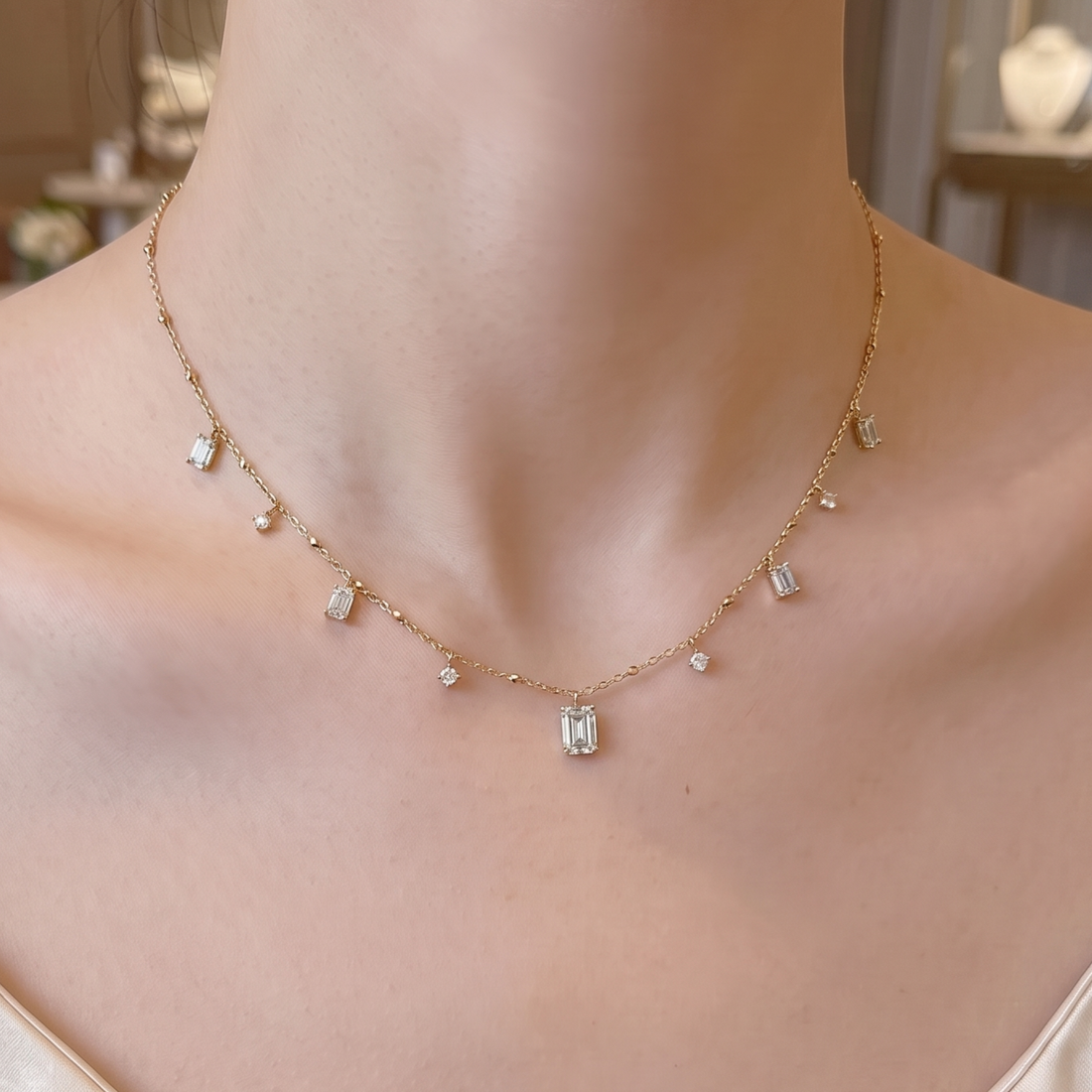 A delicate gold necklace with small clear rectangular and round stones, worn on a model's neck and upper chest.