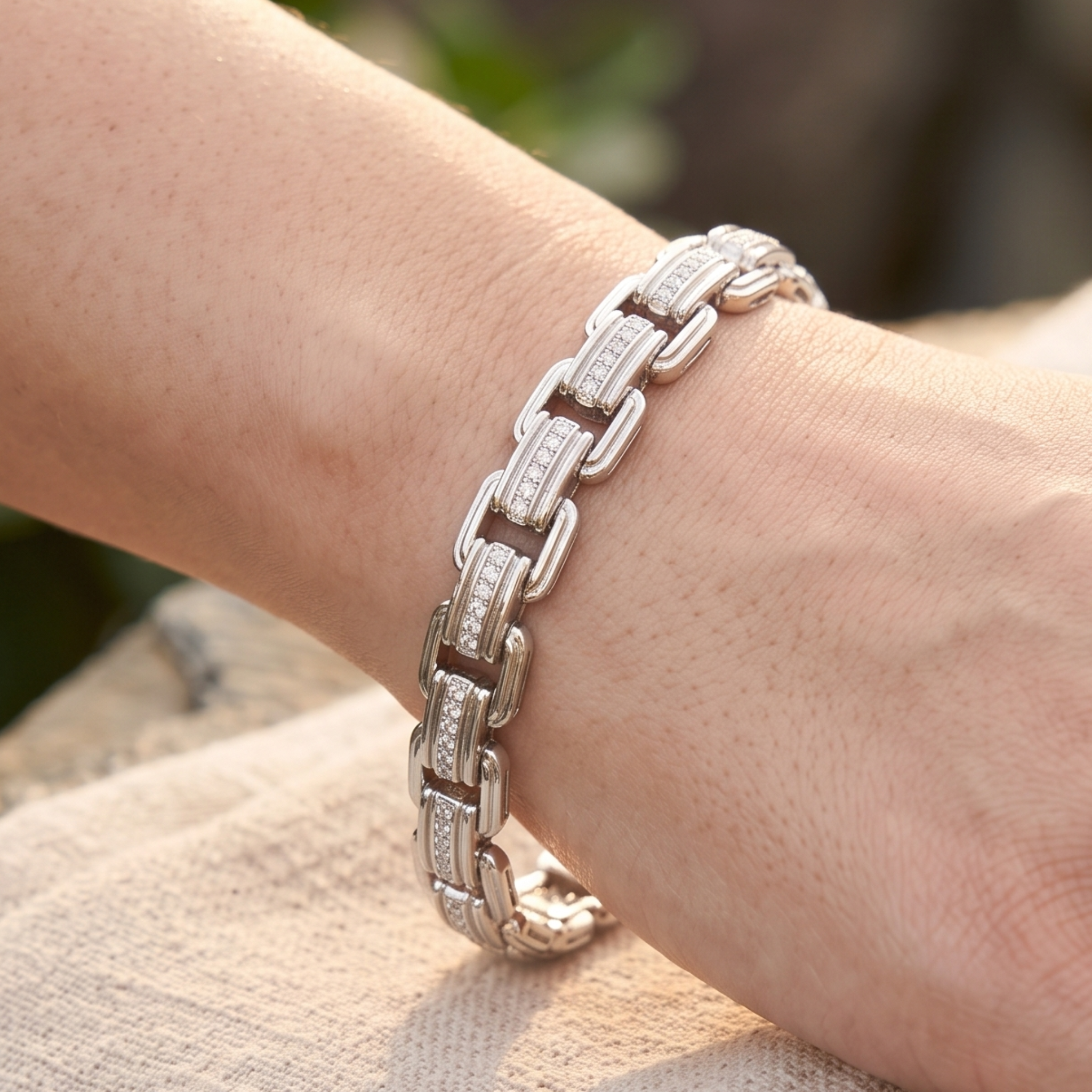 A silver-toned chain bracelet with clear pavé-set stones worn on a person's wrist, shown in a close-up lifestyle shot against a softly blurred outdoor background.
