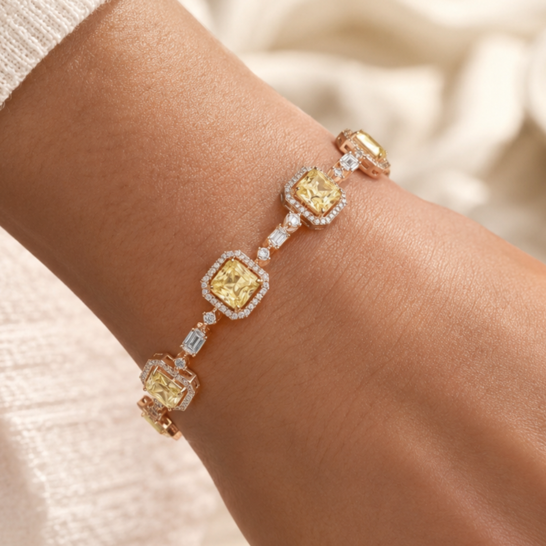A close-up of a gold bracelet with four yellow cushion-cut center stones and surrounding clear pavé accents, worn on a person's wrist against a soft cream background.