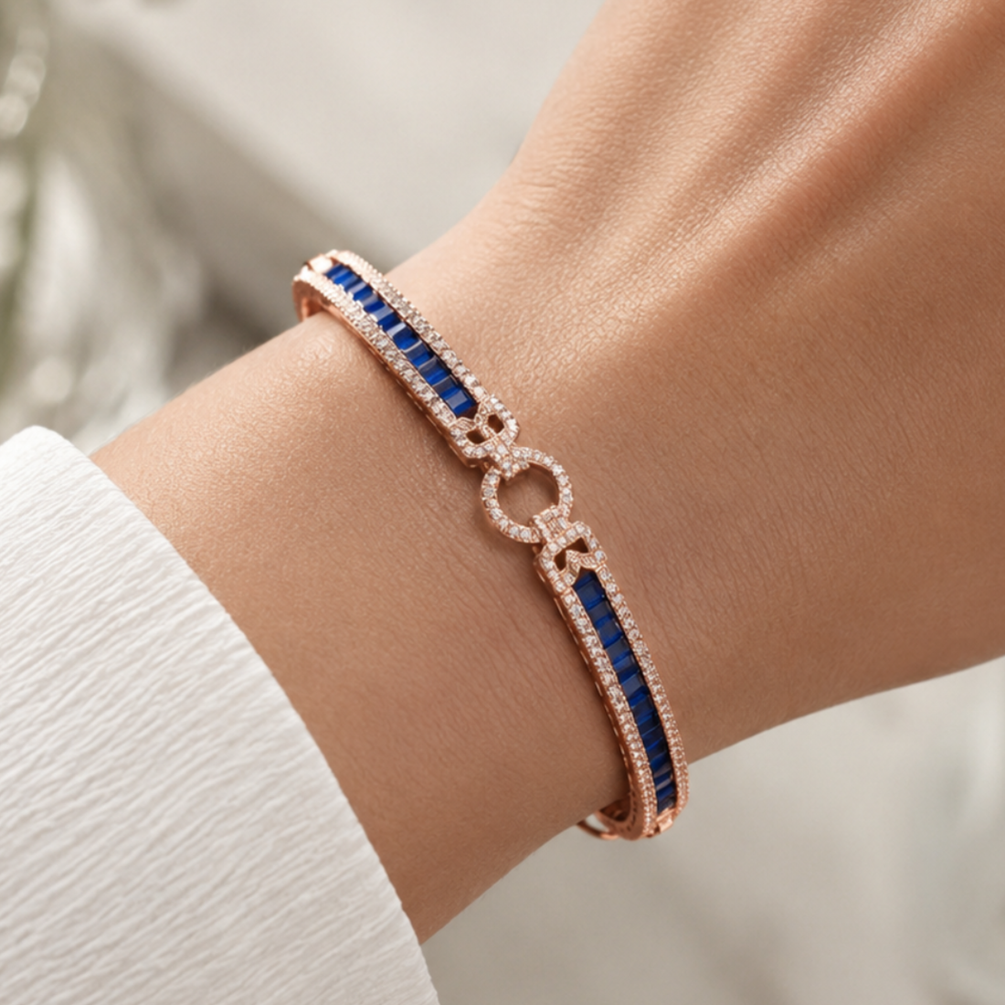 A close-up of a rose gold bracelet with deep blue rectangular stones and pavé-set clear stones, worn on a person's wrist.