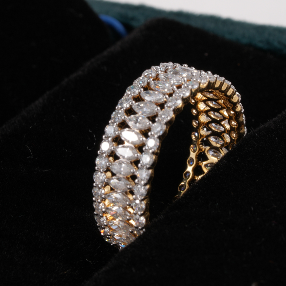 A wide gold band ring heavily set with marquise-cut clear stones, displayed on a black velvet jewelry box.