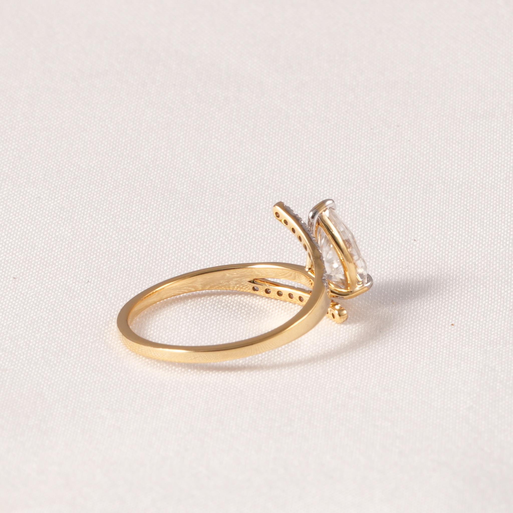 A gold ring with a marquise-cut clear gemstone in a prong setting, photographed on a light beige textured fabric background.