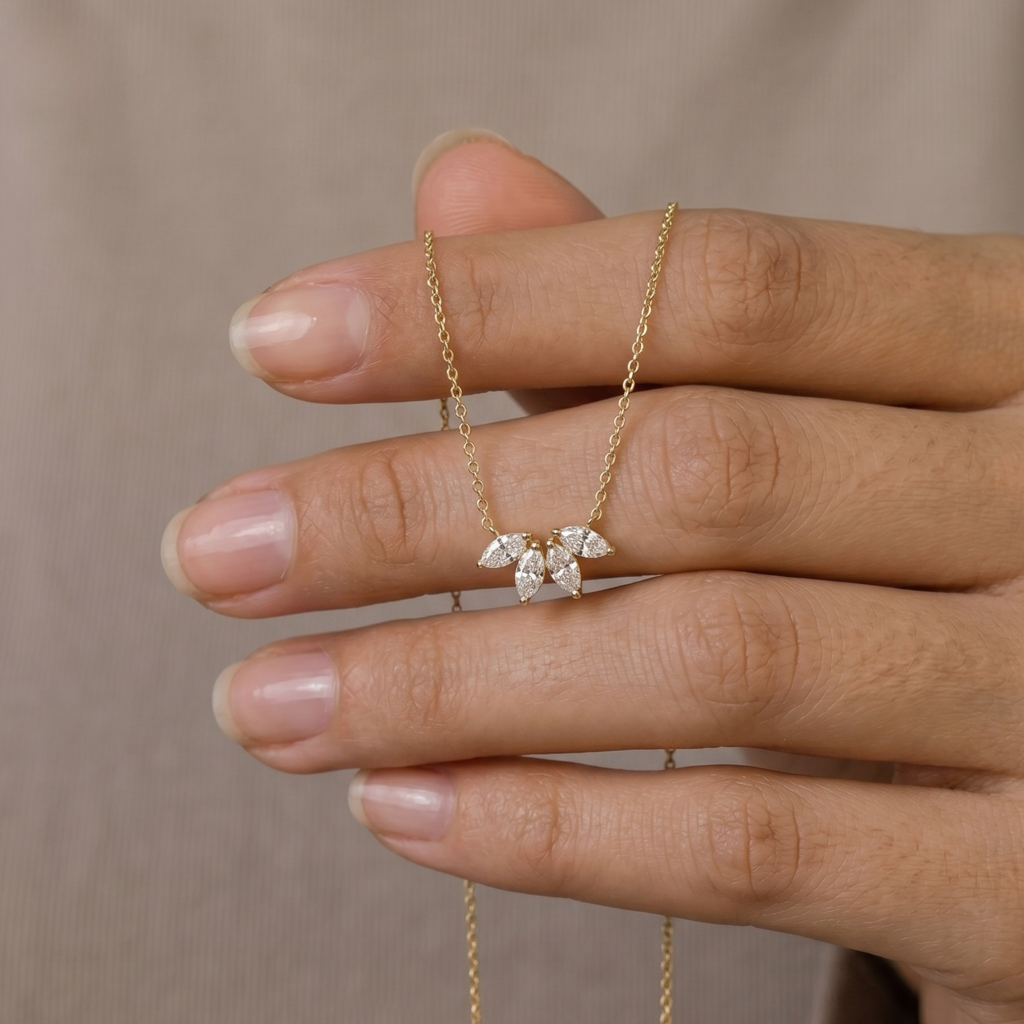 A delicate gold chain necklace with a small bow-shaped crystal pendant, held on a person's fingers against a soft beige background.