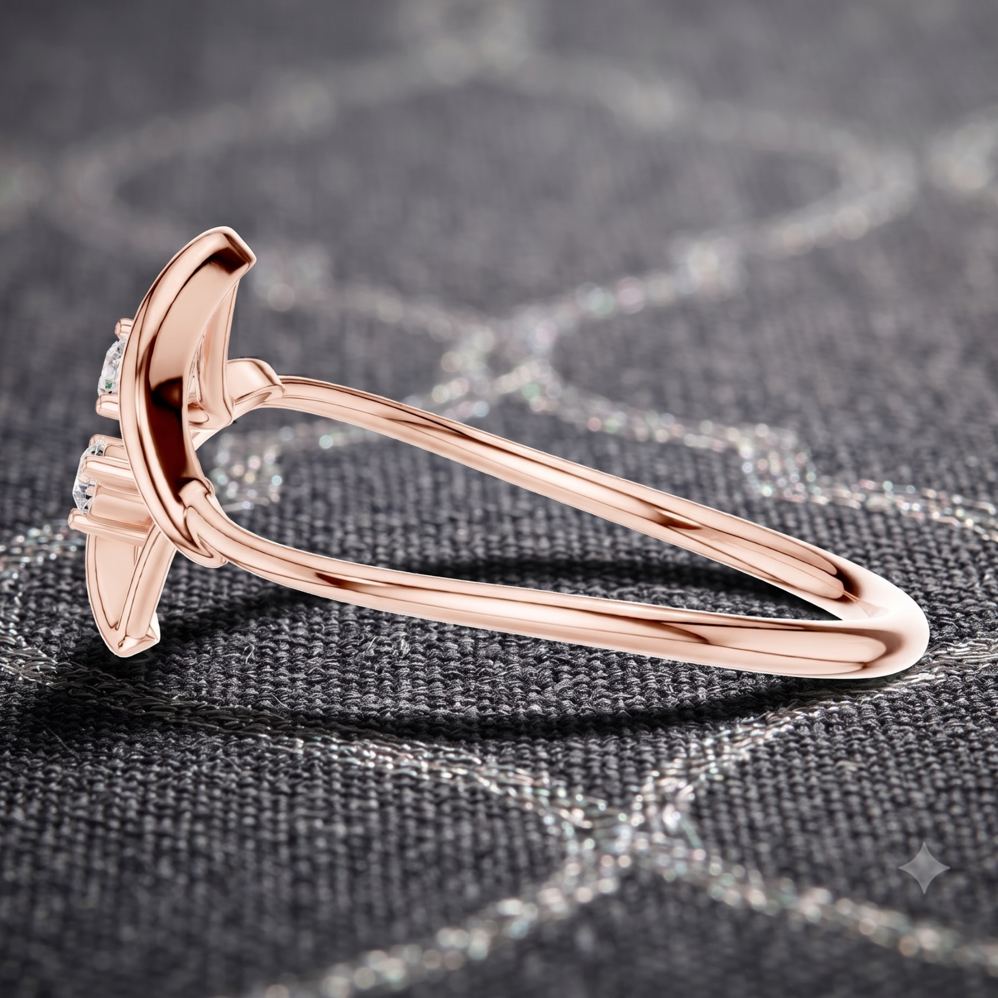 A rose gold ring with a curved, sculptural setting and small clear gemstones, resting on a dark gray textured fabric background.